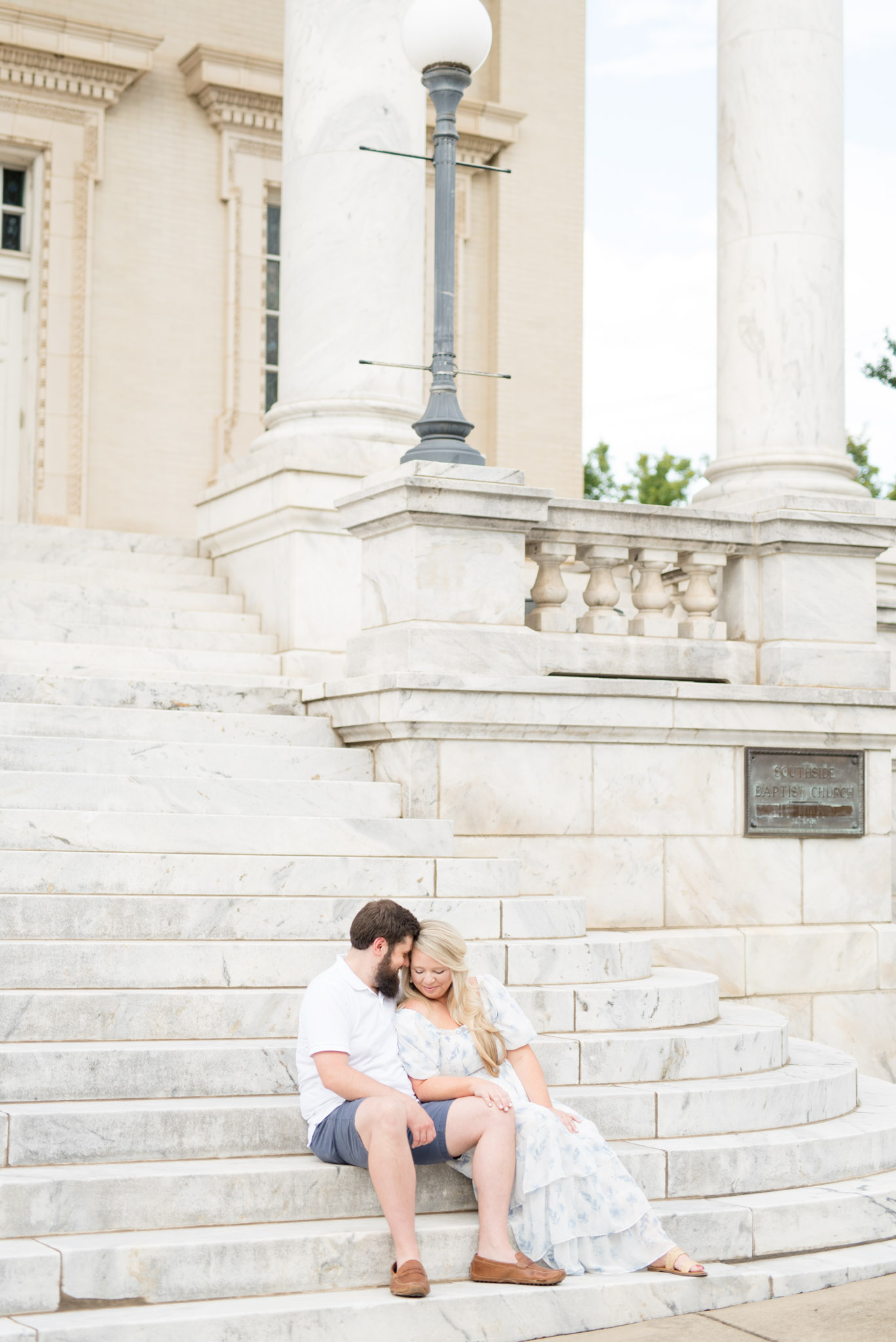 Husband snuggles wife as they sit on marble stairs.
