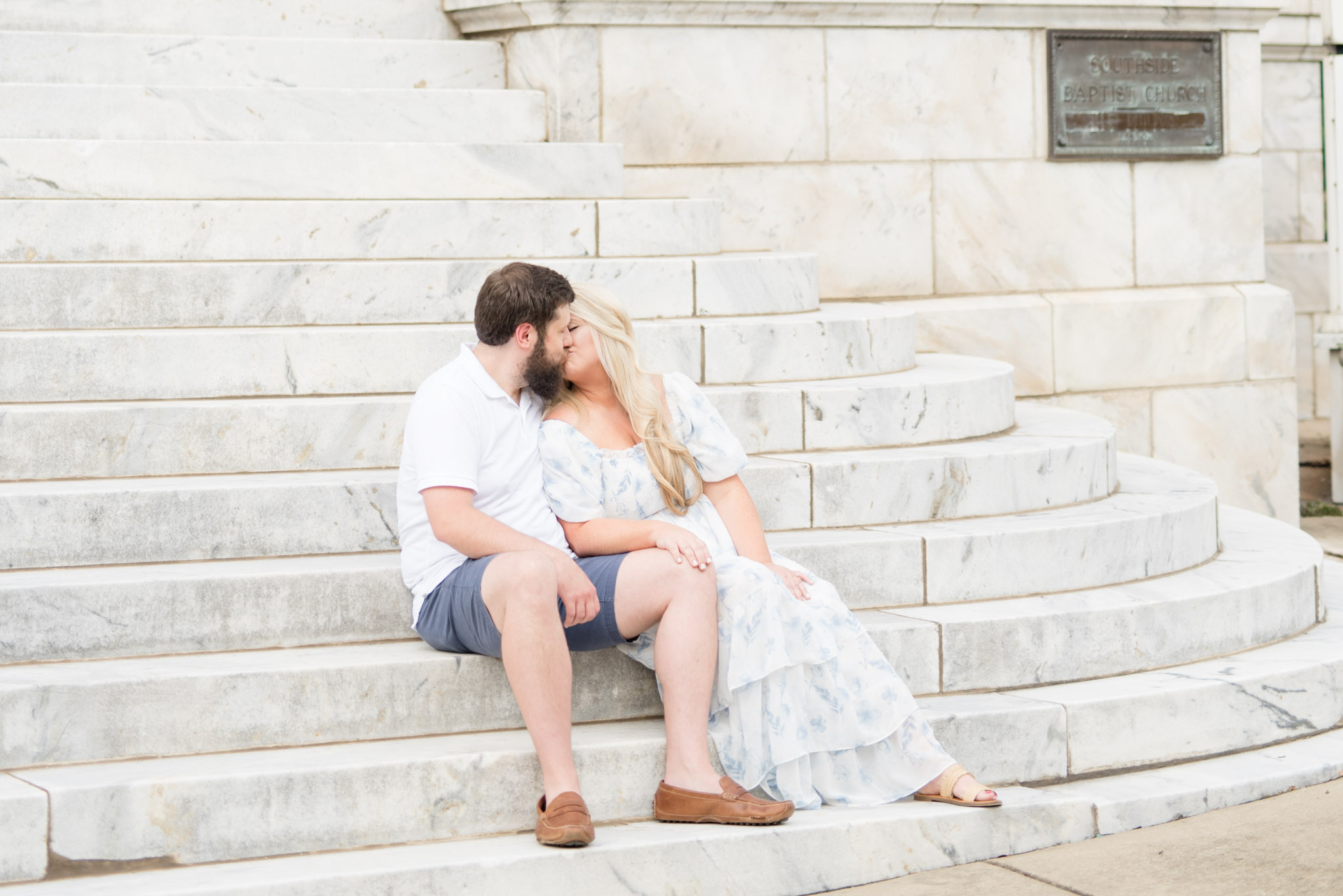Married couple kisses while sitting on marble stairs.