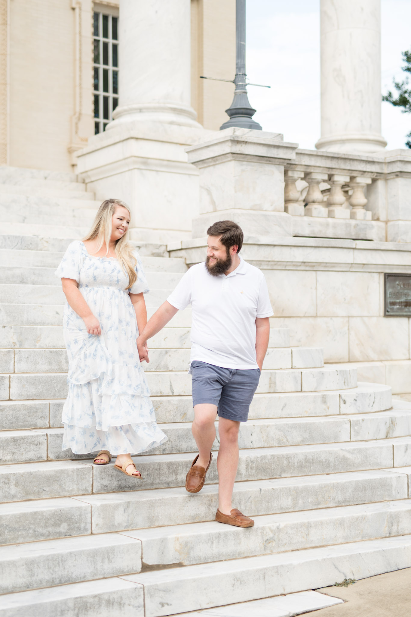 Married couple walk down marble stairs.