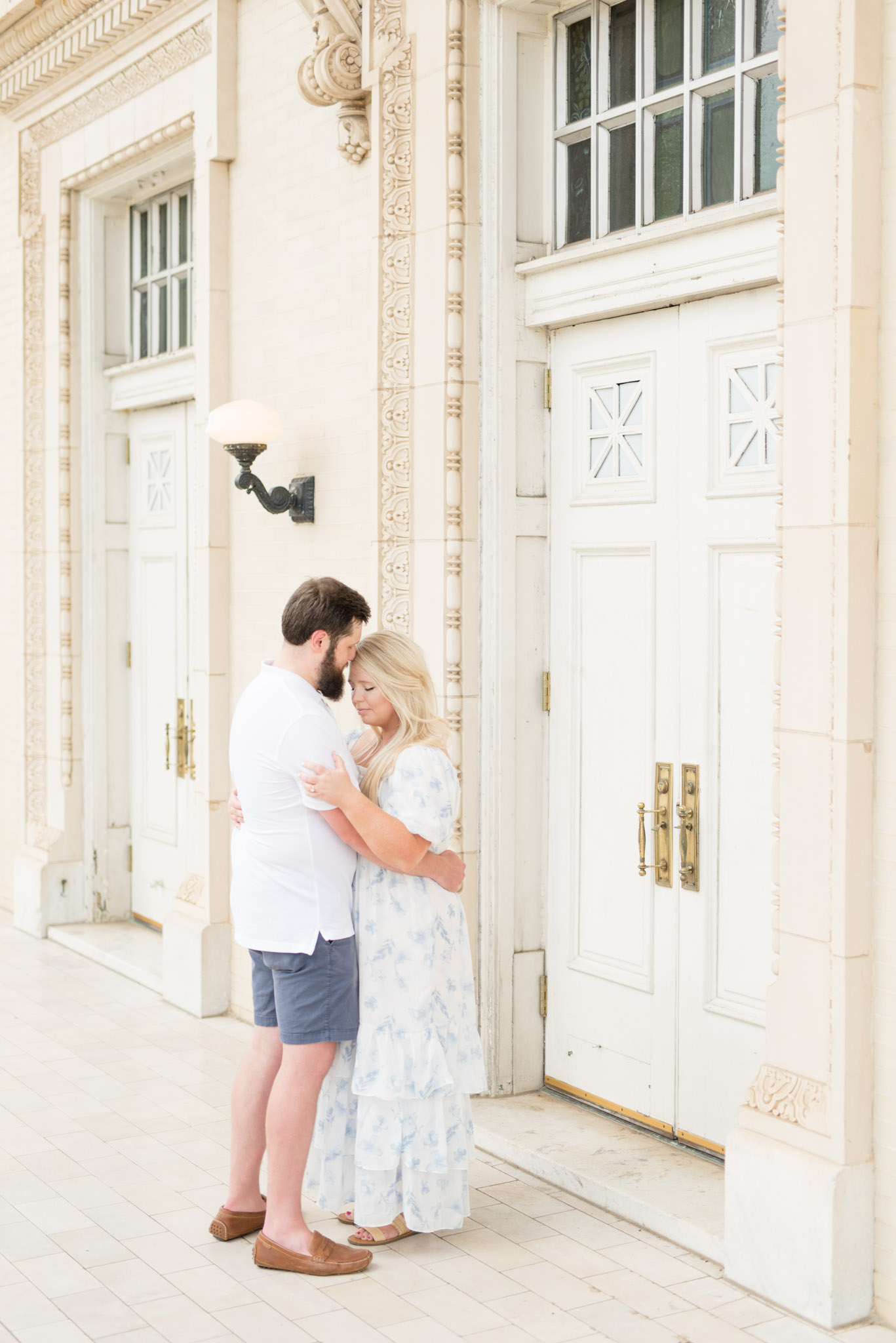 Husband and wife snuggle by large white doors.