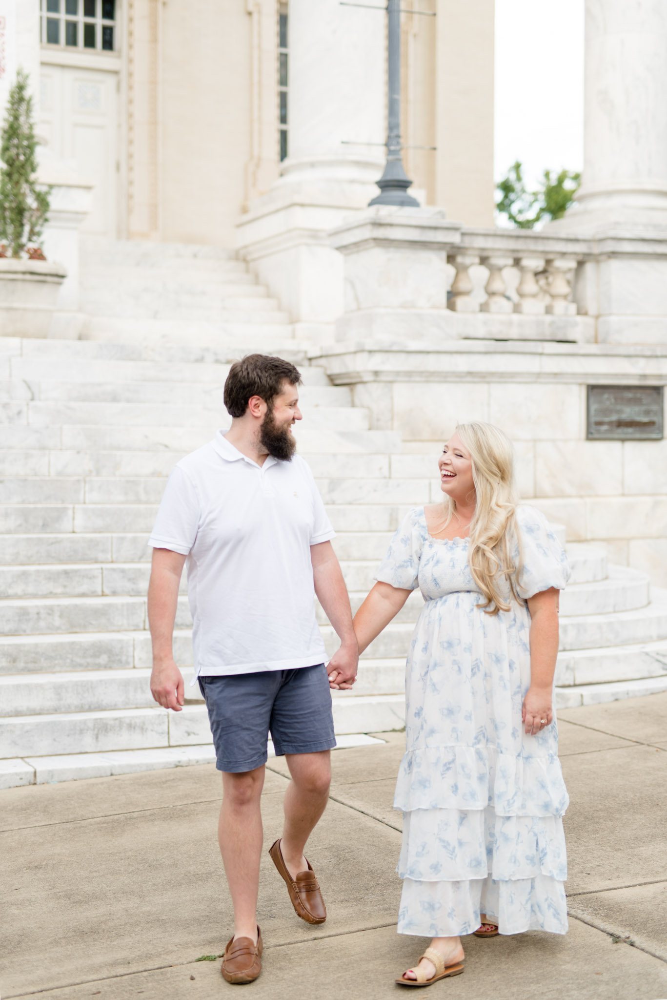 Couple walks together in front of white stairs.