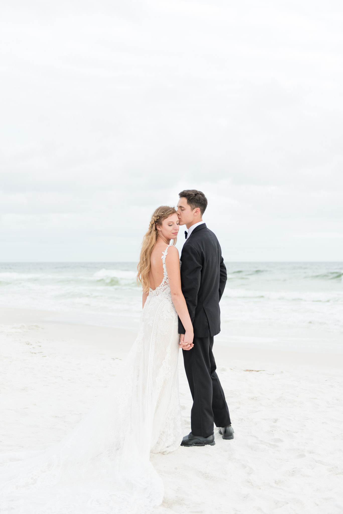 Groom kisses bride on temple on beach.