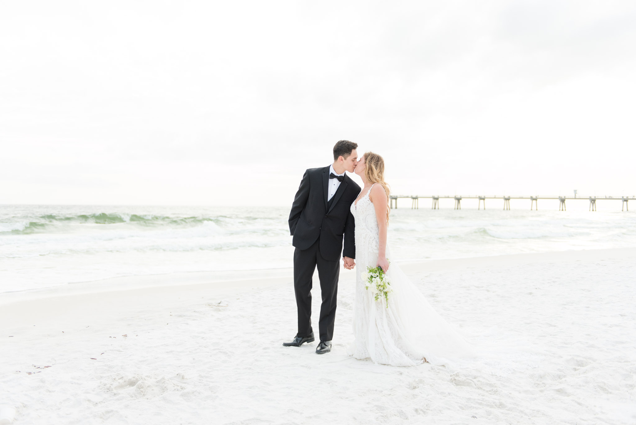Bride and groom lean in for kiss on beach.