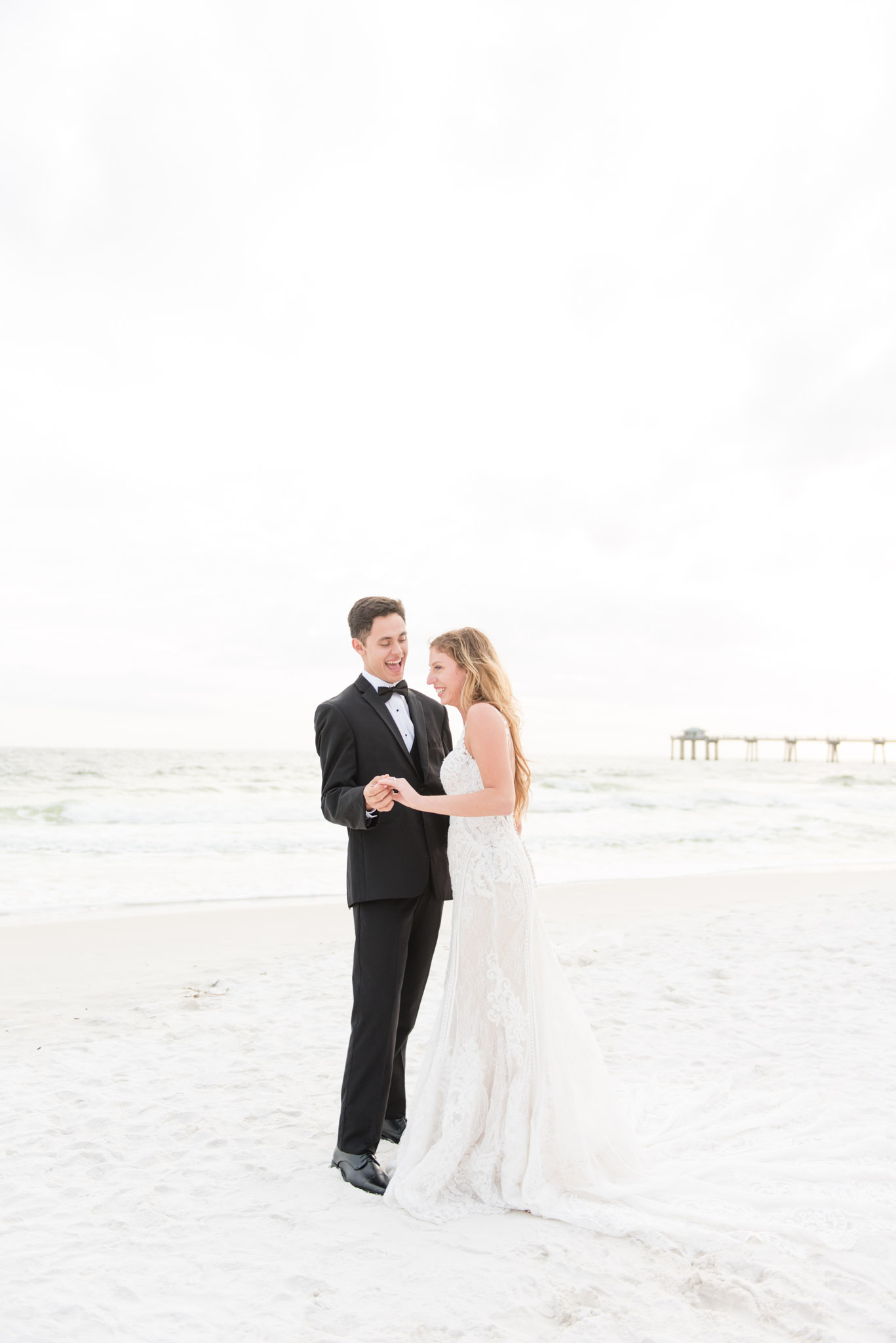 Bride and groom laugh by ocean.