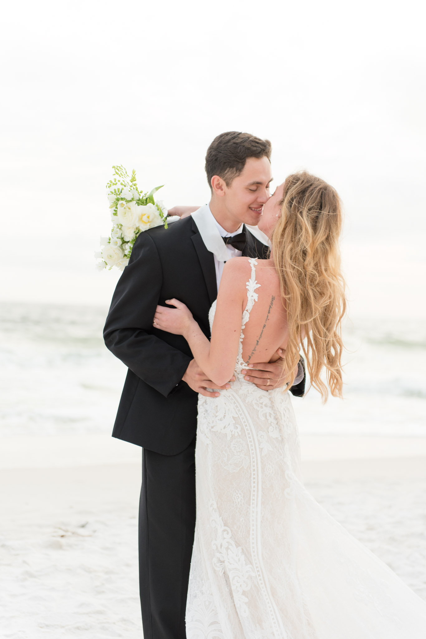 Groom leans in to kiss bride at sunset.