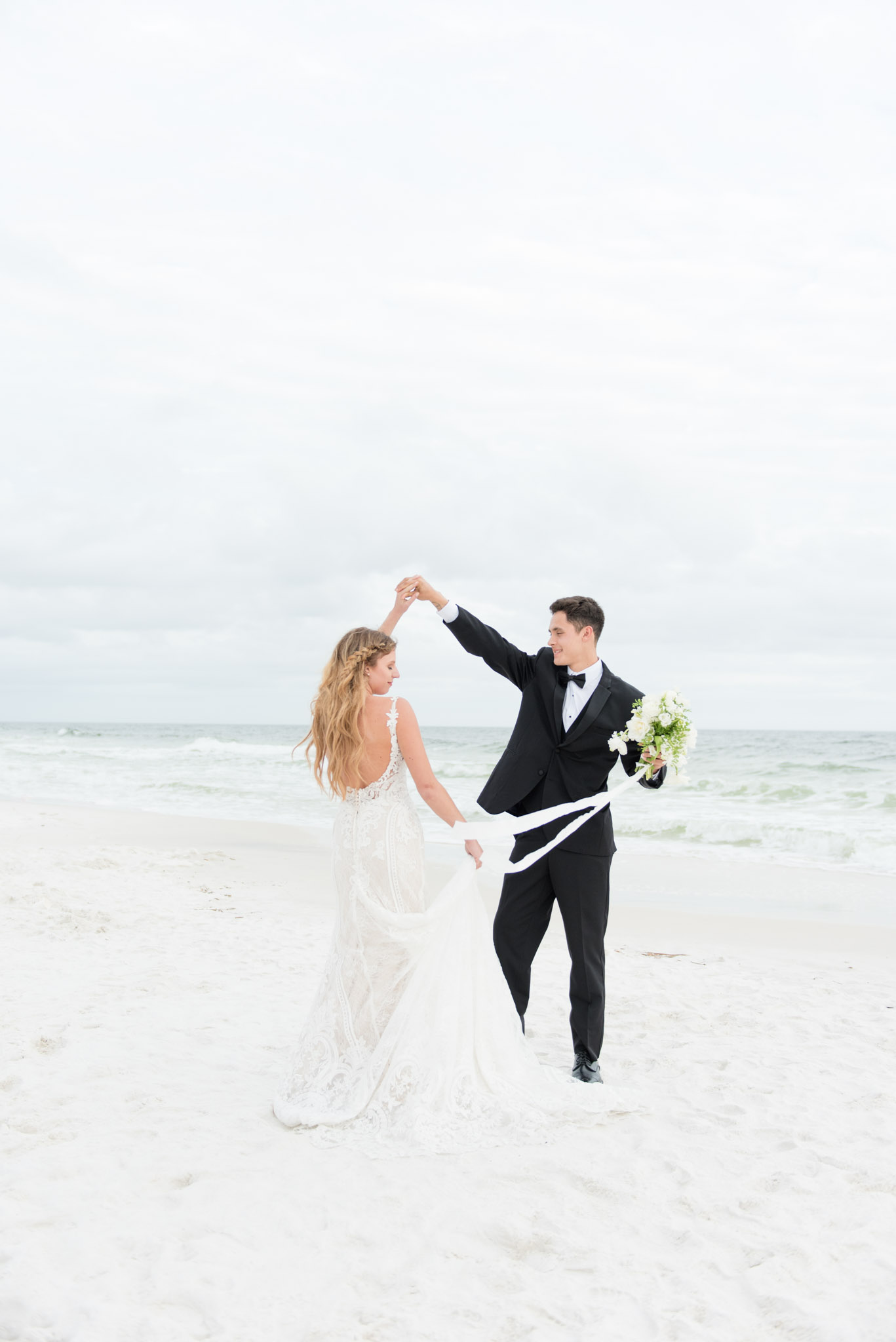 Groom twirls bride on beach.