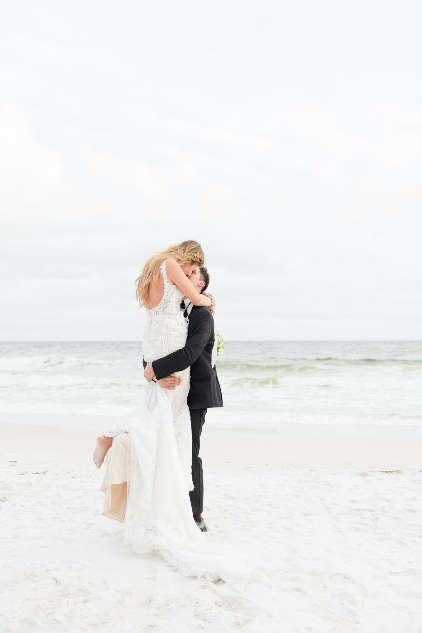 Groom picks up bride on beach.