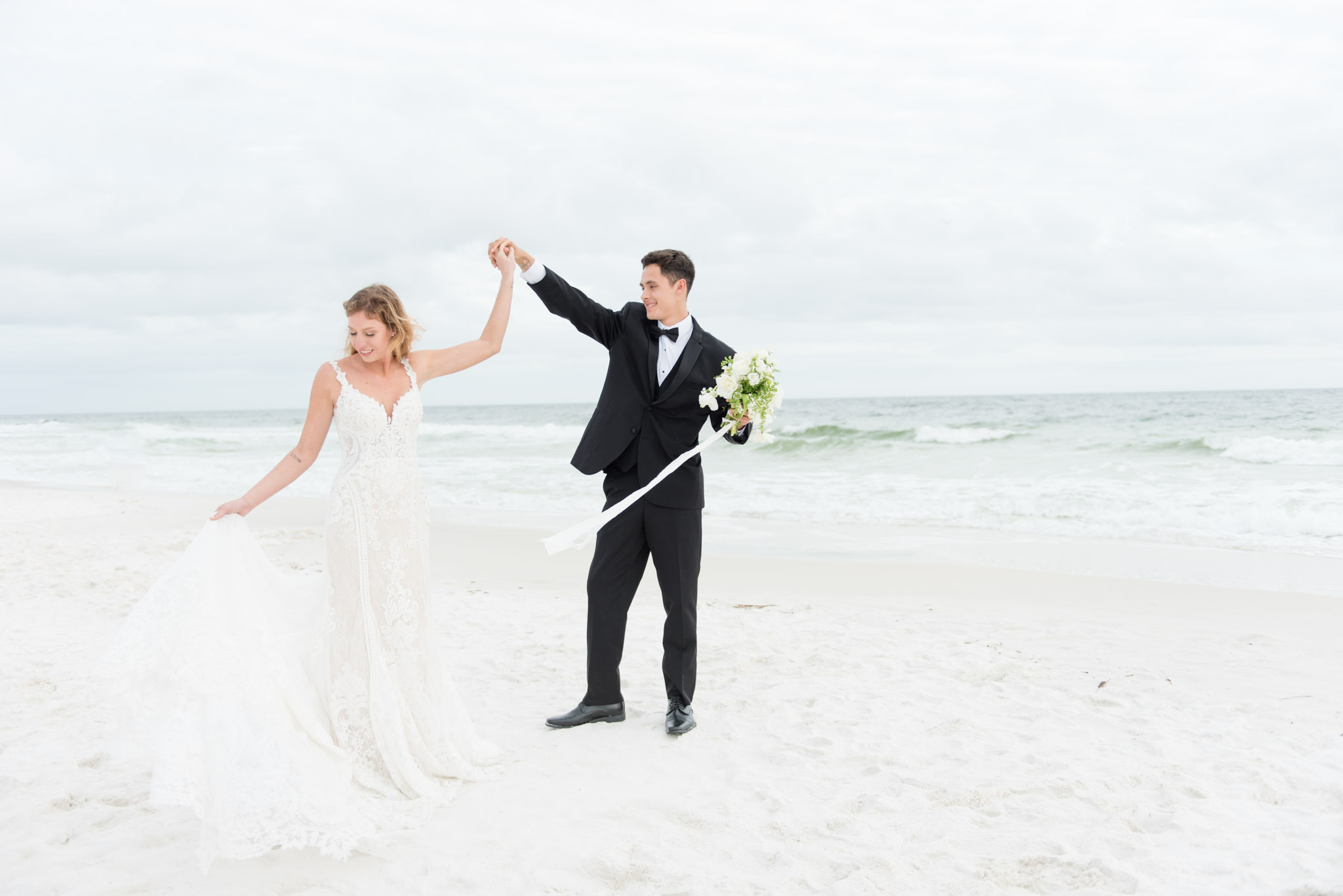 Groom twirls bride by ocean.