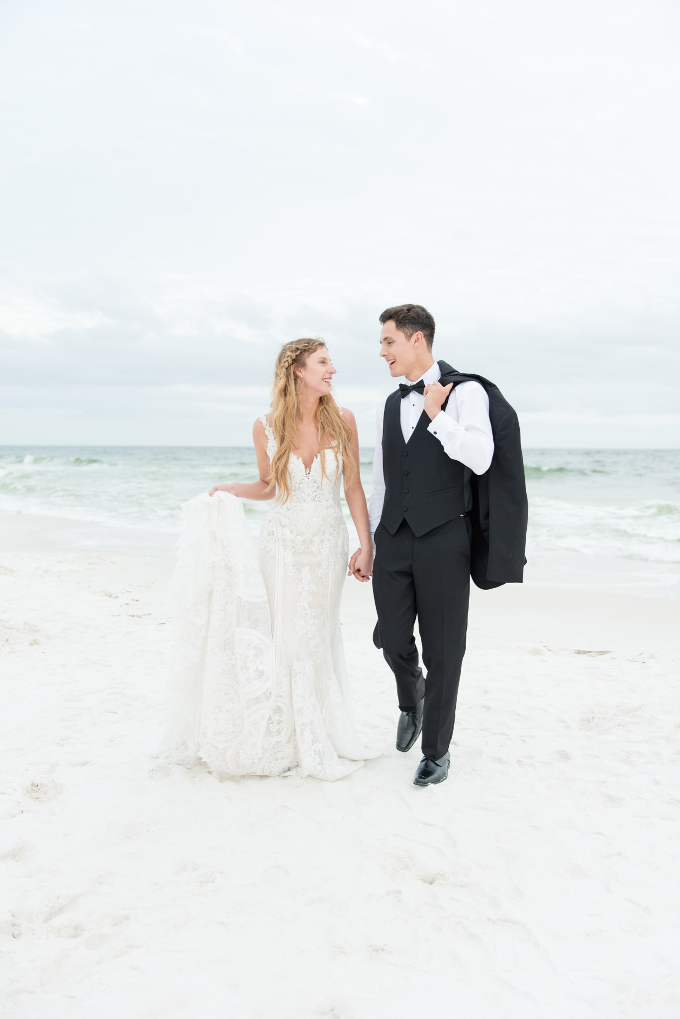Bride and groom walk by ocean.