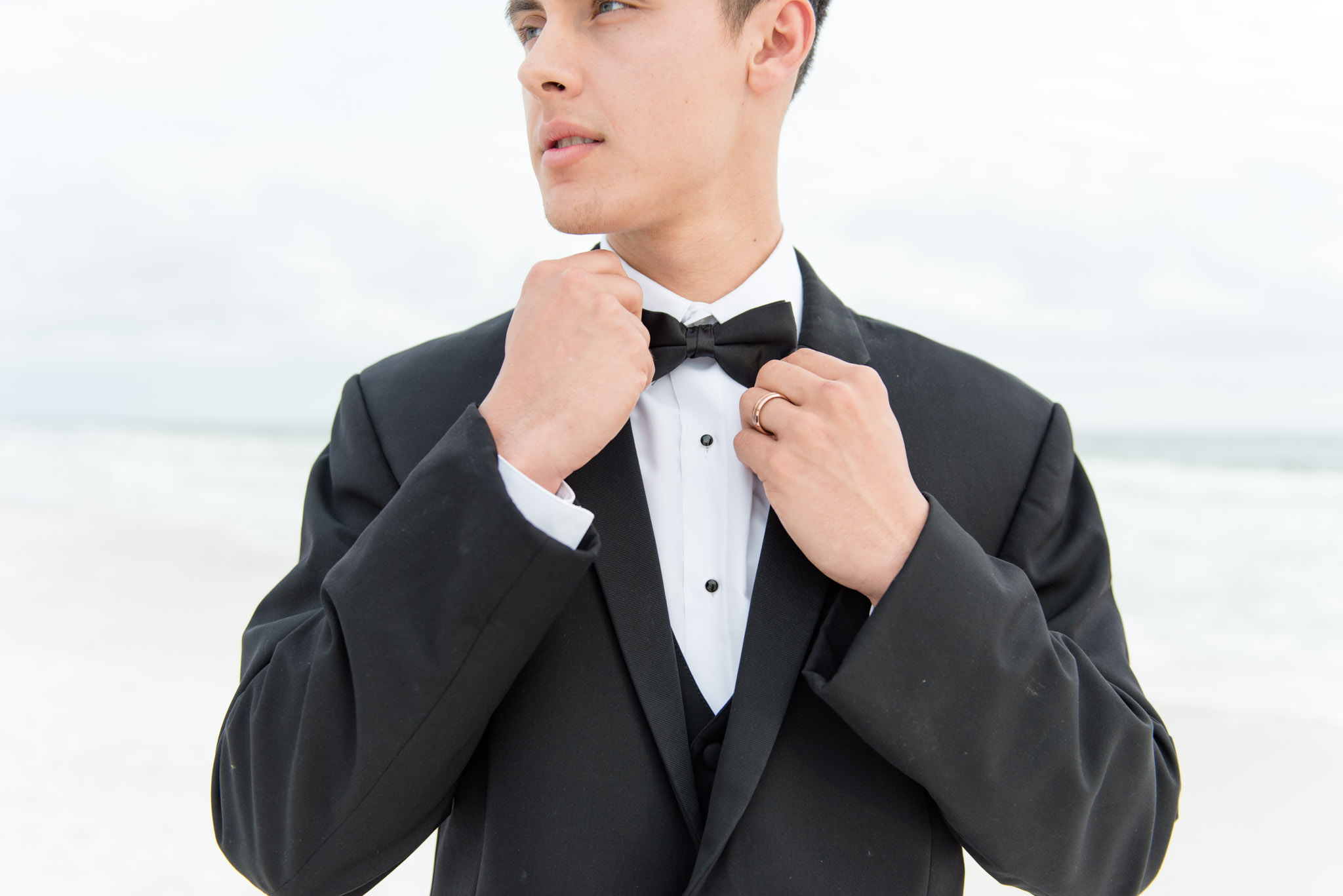 Groom straightens tie on beach.