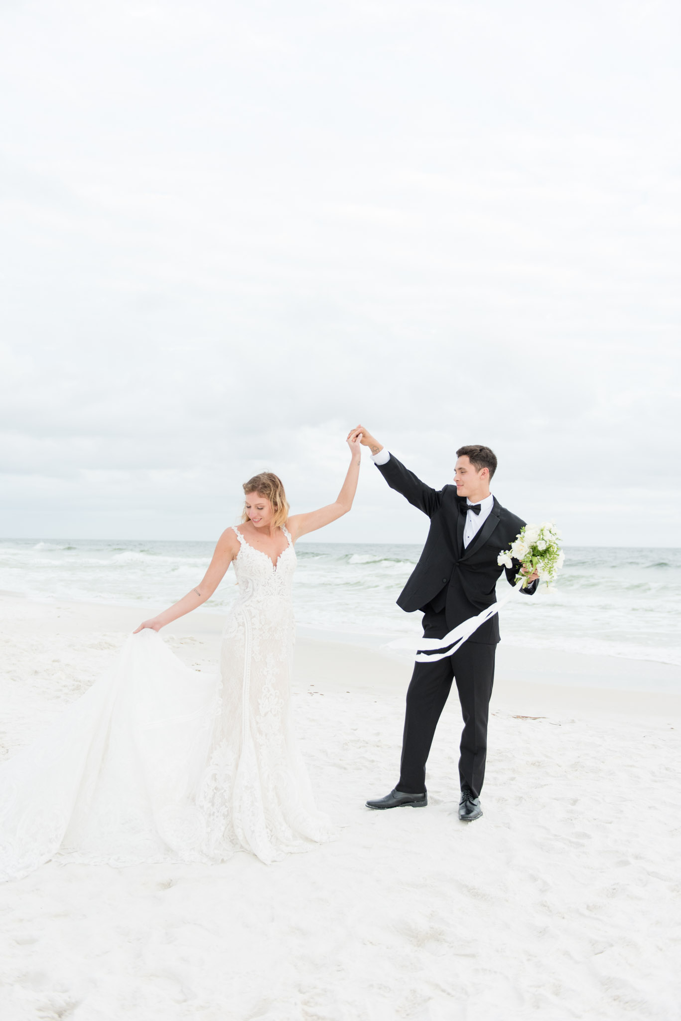 Groom twirls bride by ocean at sunset.