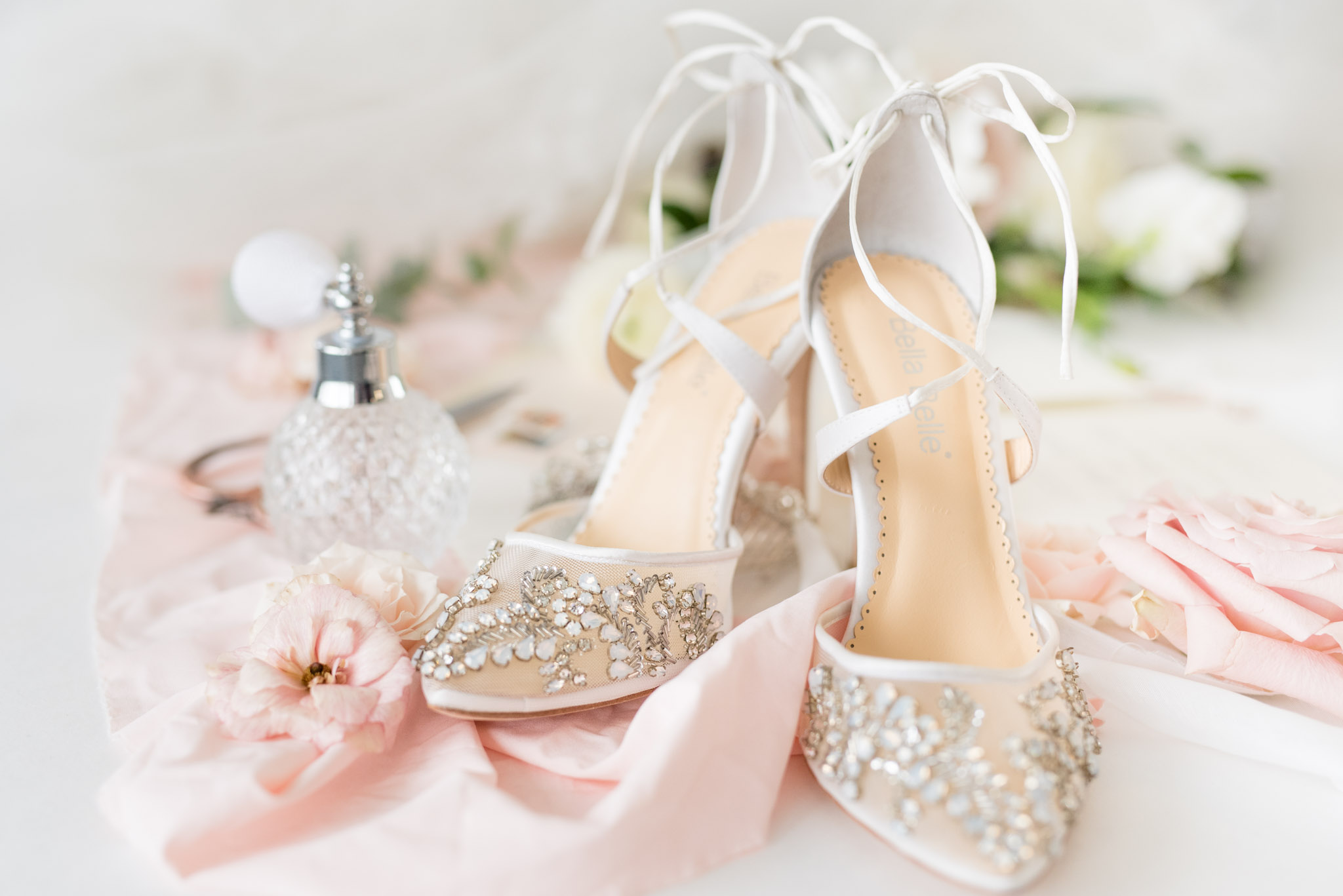 Wedding shoes sit with perfume bottle and flowers.