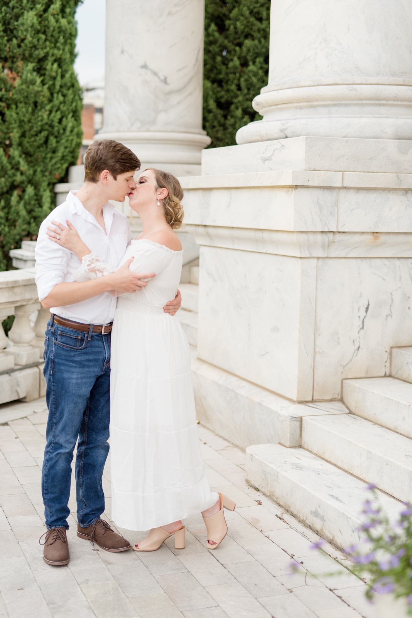 Engaged couple kiss by marble columns.