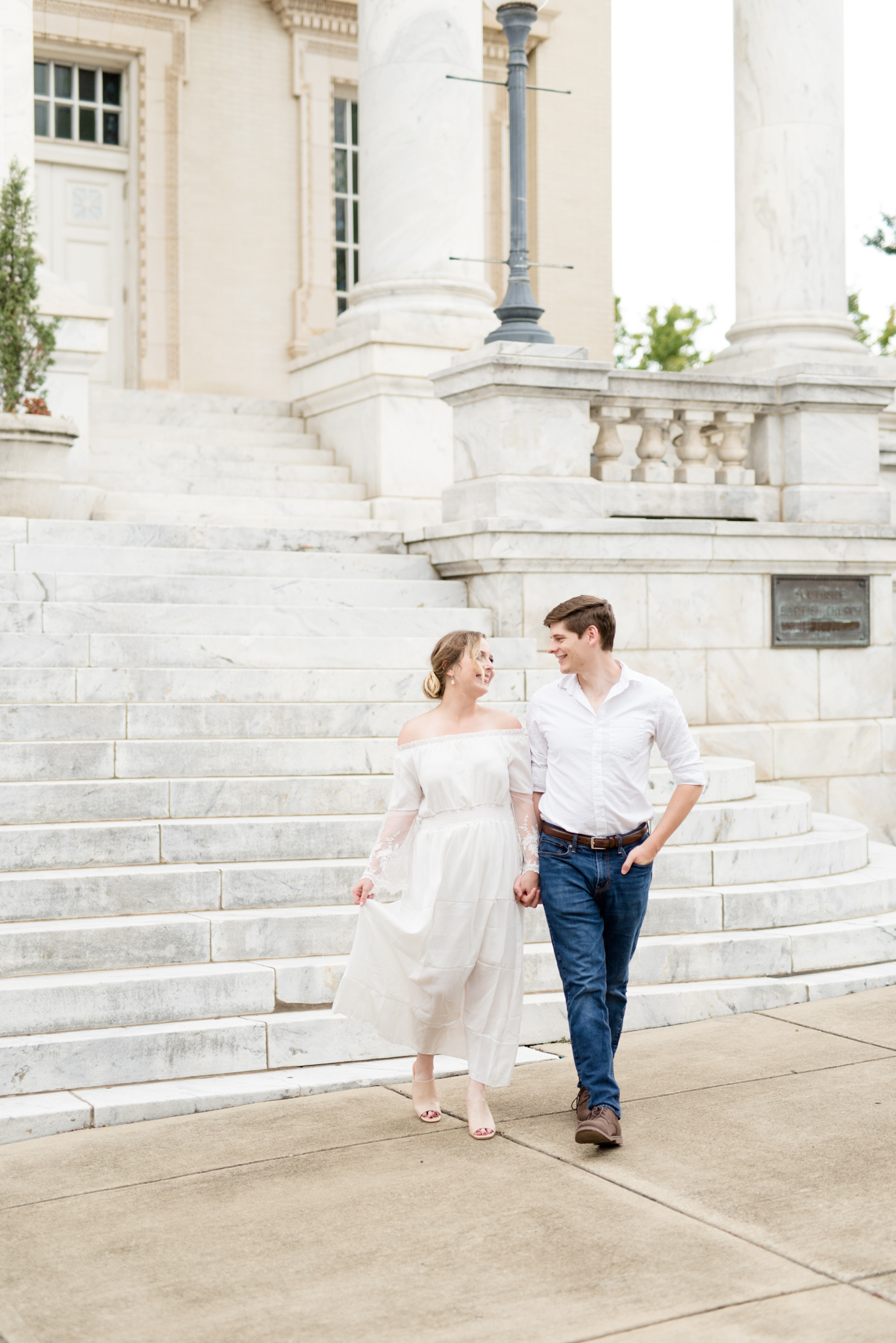 Couple walks in front of marble staircase.