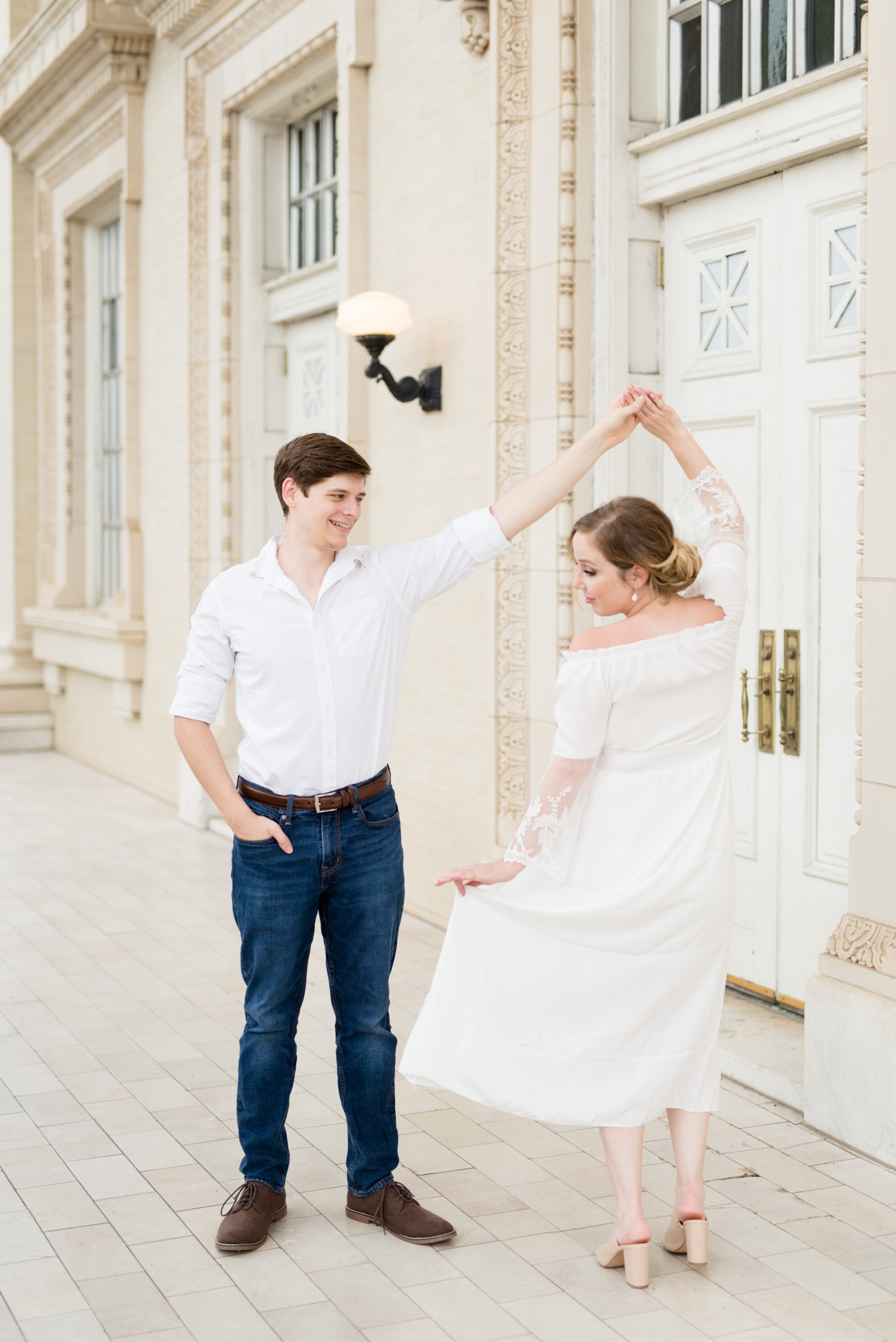 Man twirls fiance in front of white doors.
