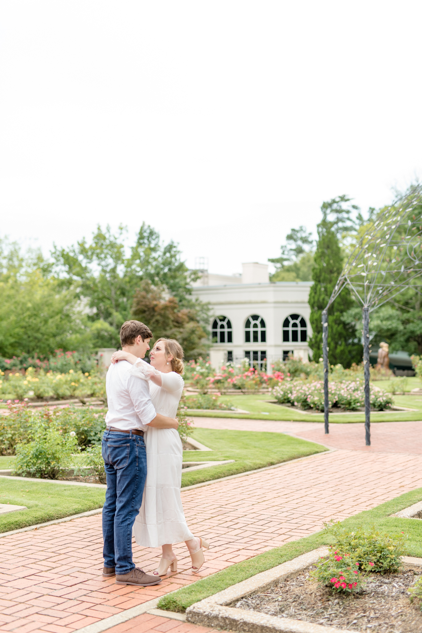 Engaged couple cuddles in rose garden.