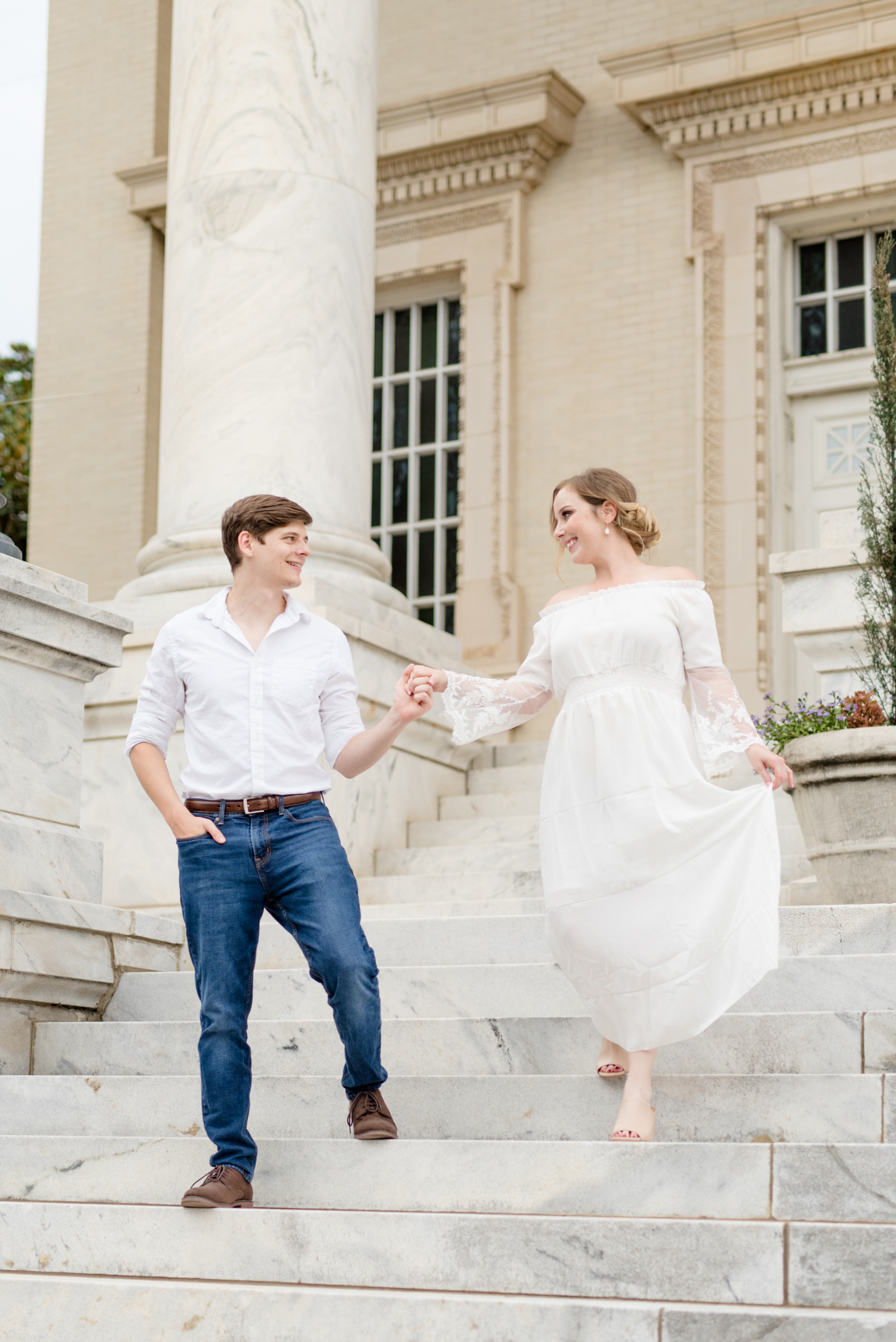Engaged couple walks down marble staircase.