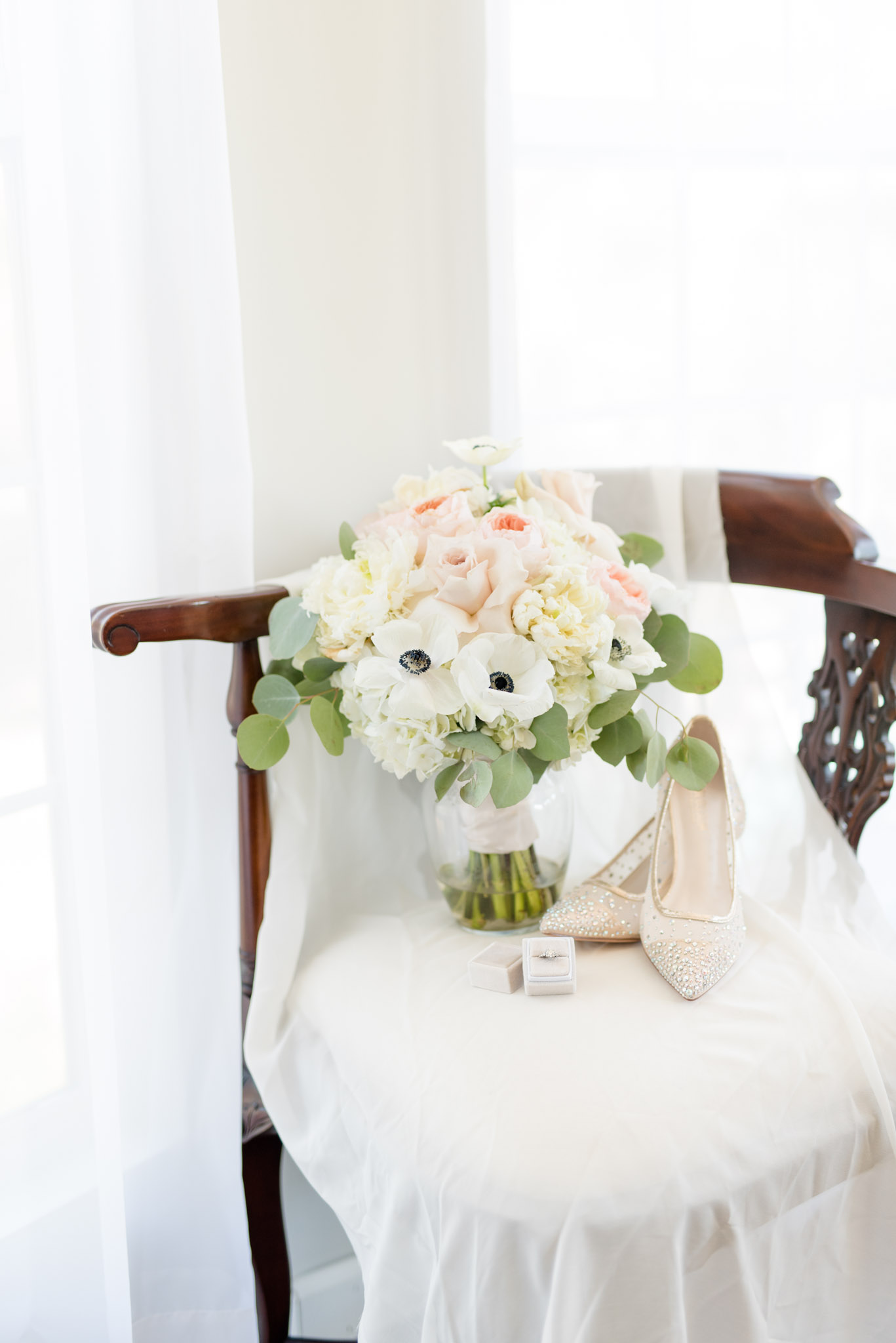 Bridal boquet, shoes, and ring sit on chair.