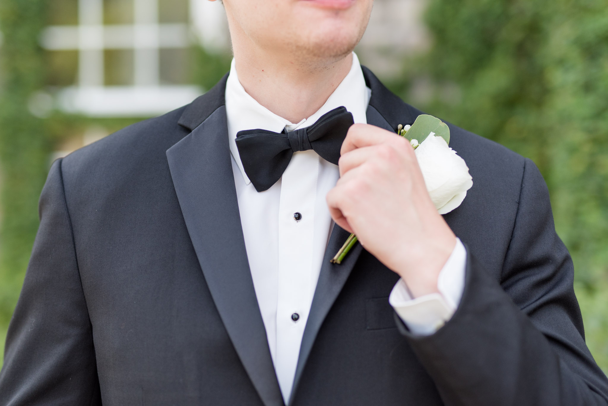 Groom straightens bow tie with hand.