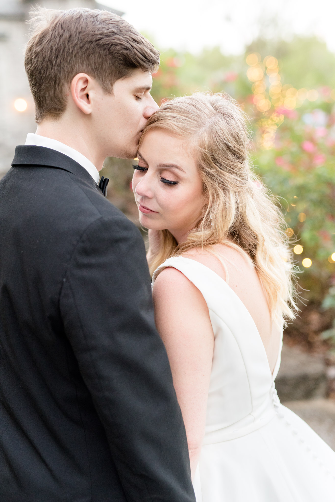 Groom kisses bride on forehead.