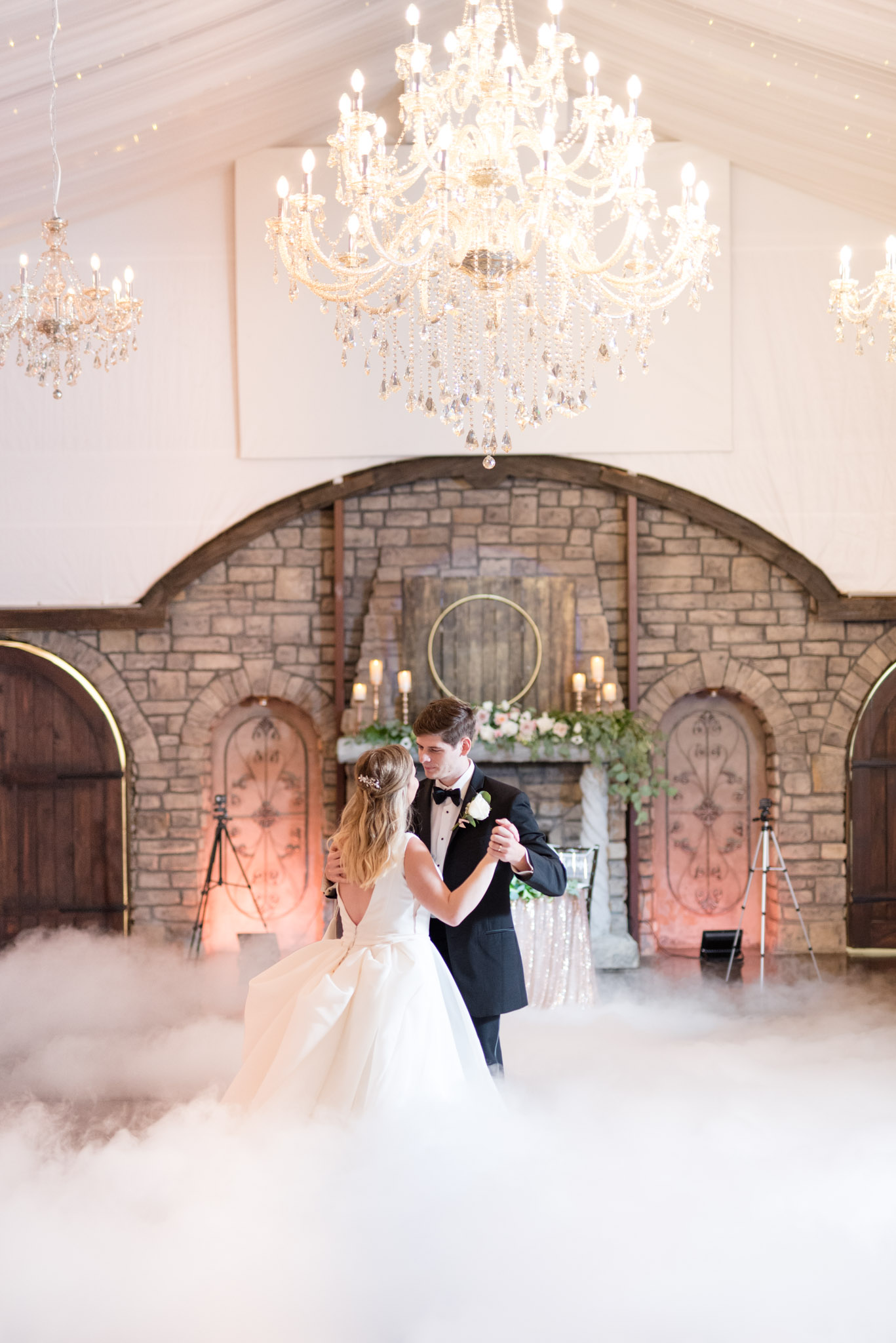 Bride and groom dance under chandelier.