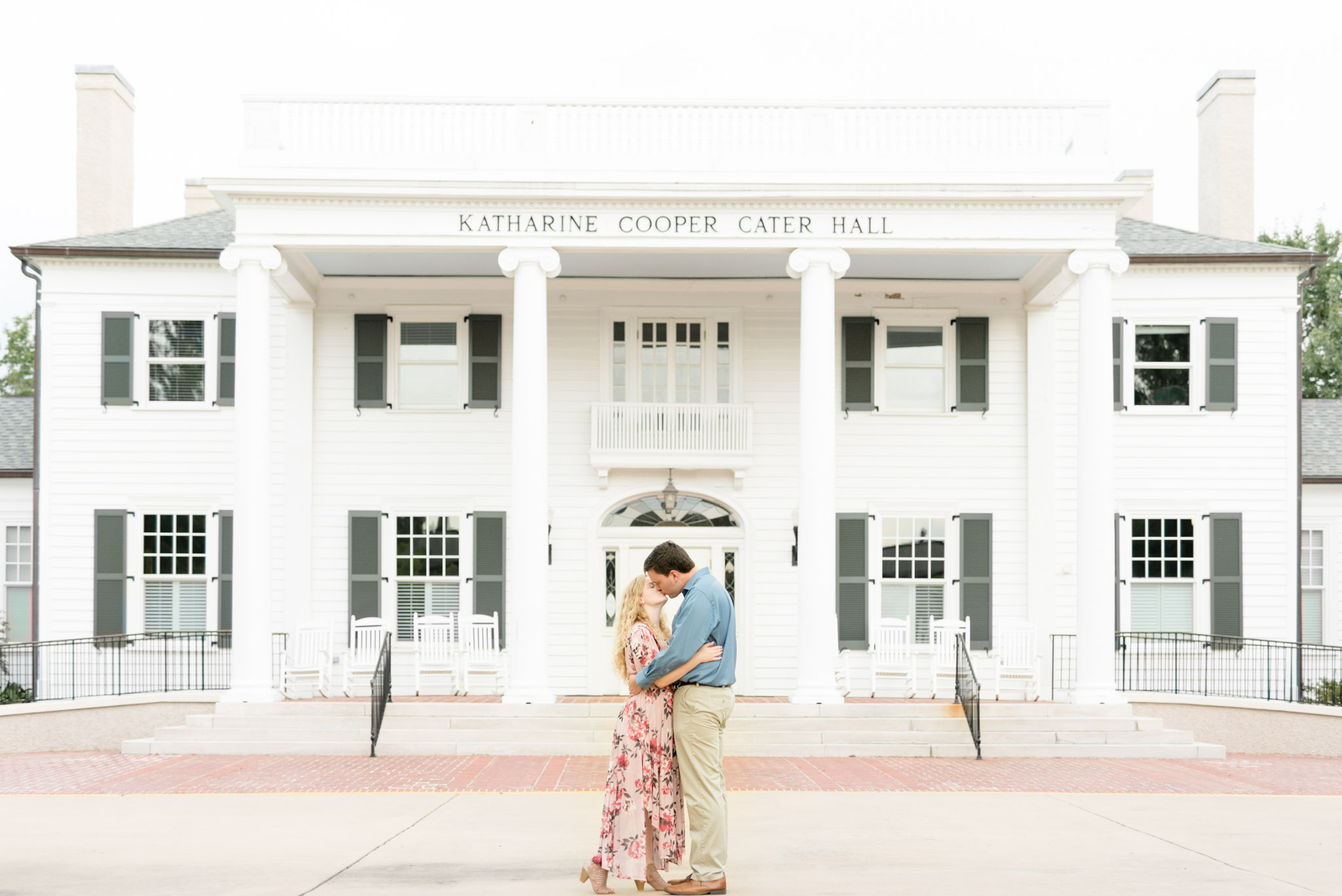 Couple kisses in front of white mansion.