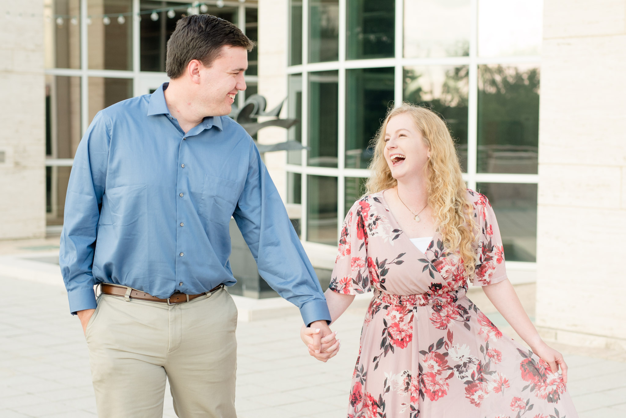 Engaged couple laughs together while holding hands.