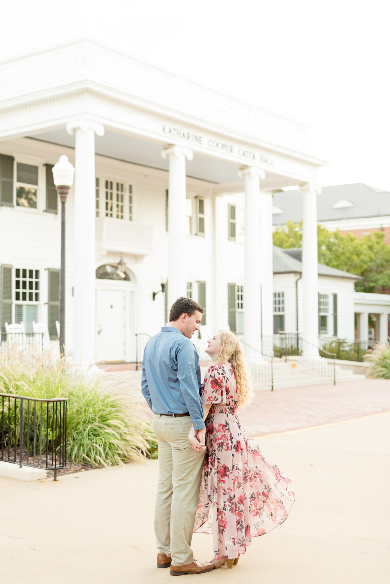 Engaged couple stands in front of white building.