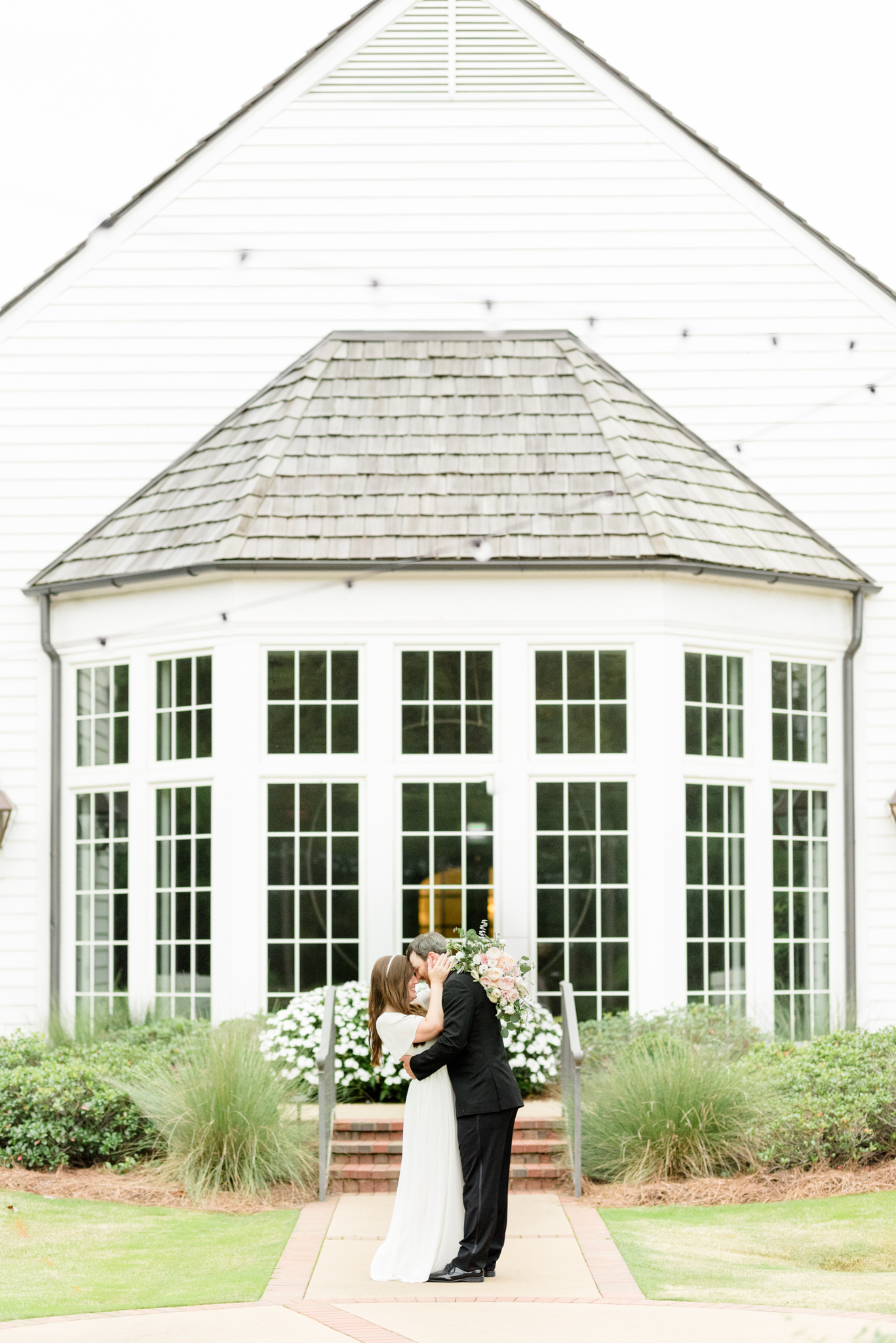 Couple cuddles in front of white building.