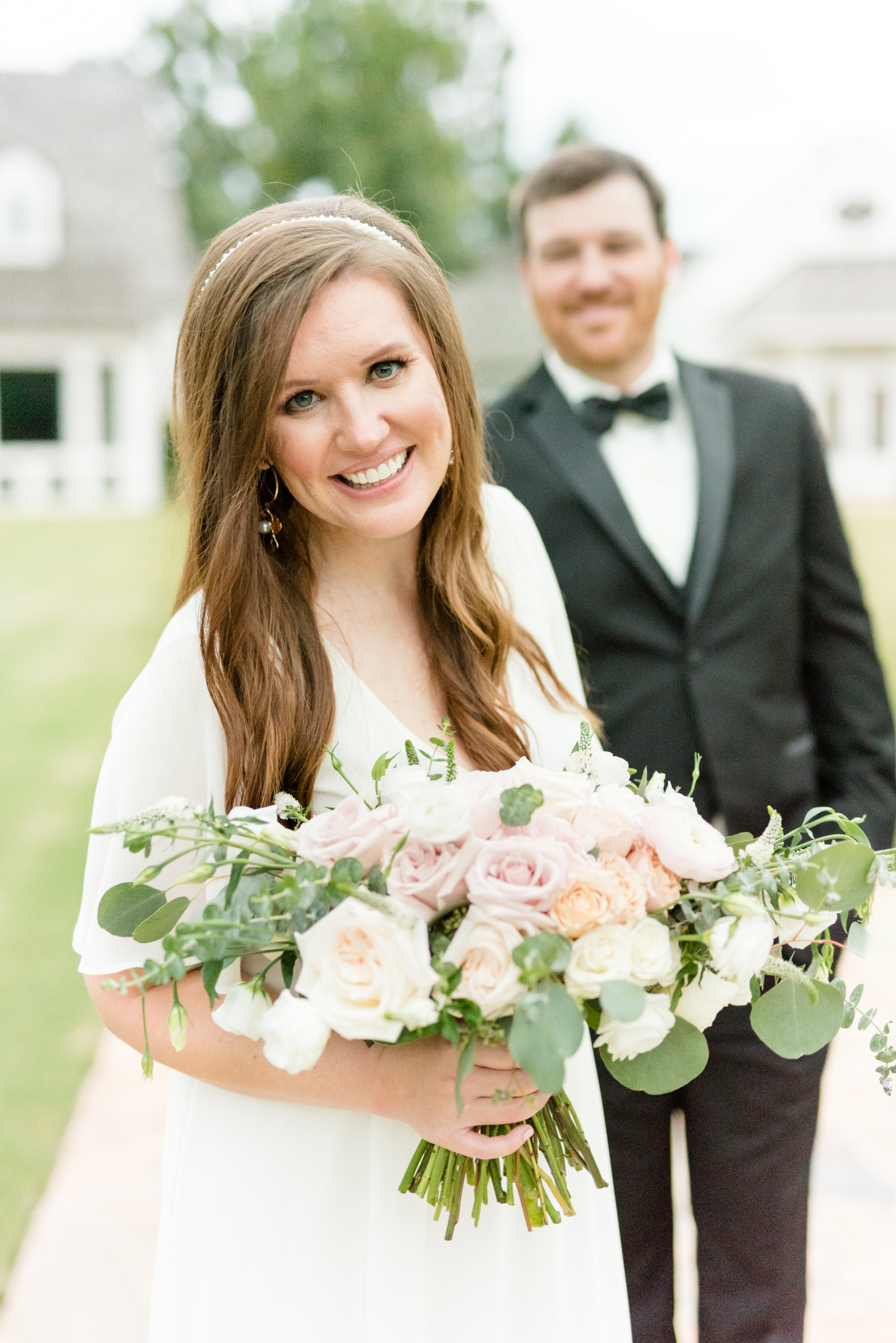 Bride leans towards camera and smiles while holding groom's hand.