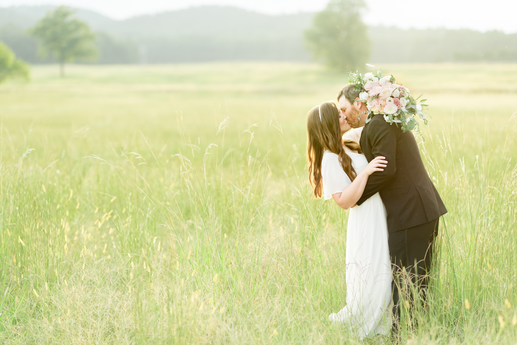 Bride and groom kiss at sunset in field.