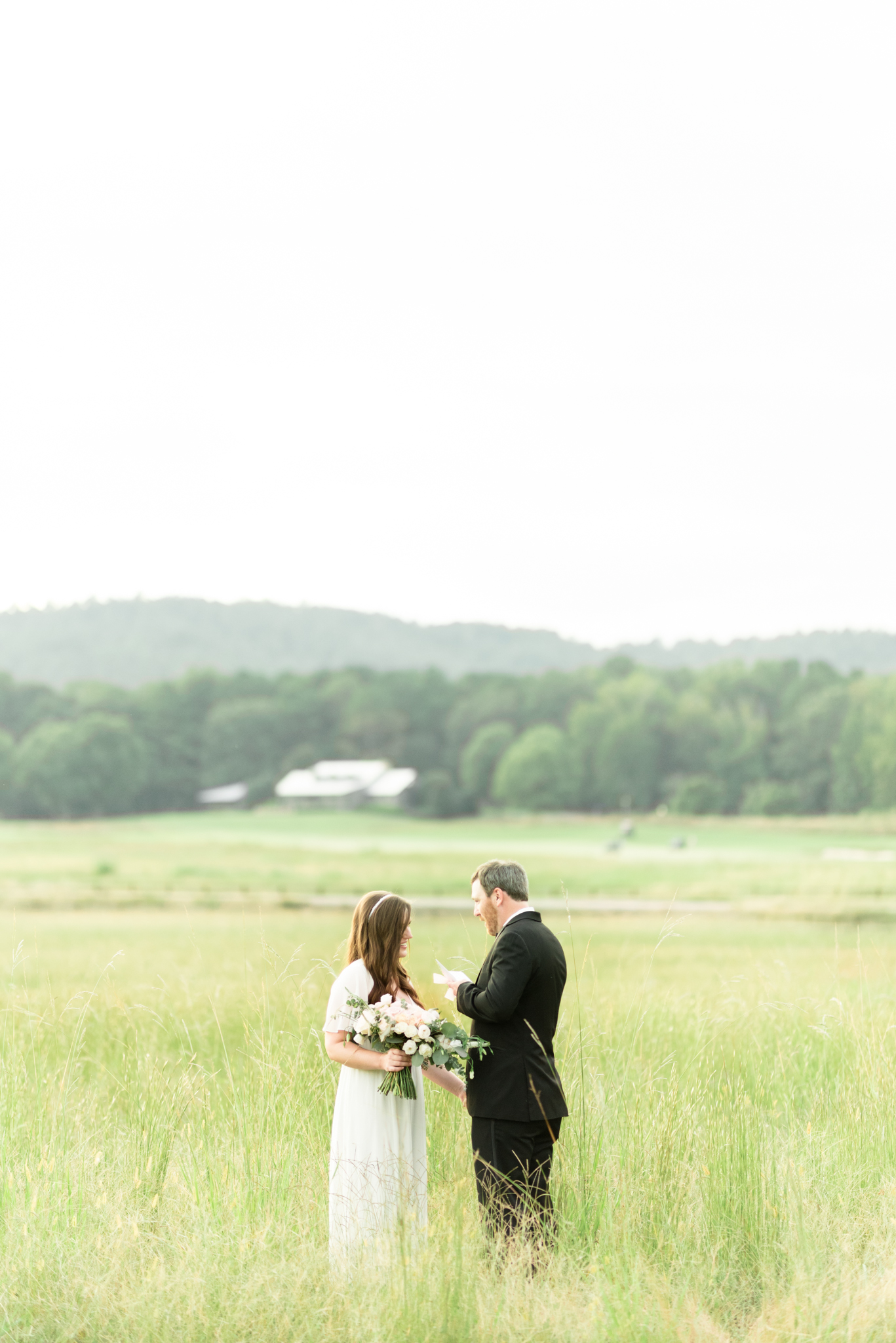 Bride and groom read vows in field.