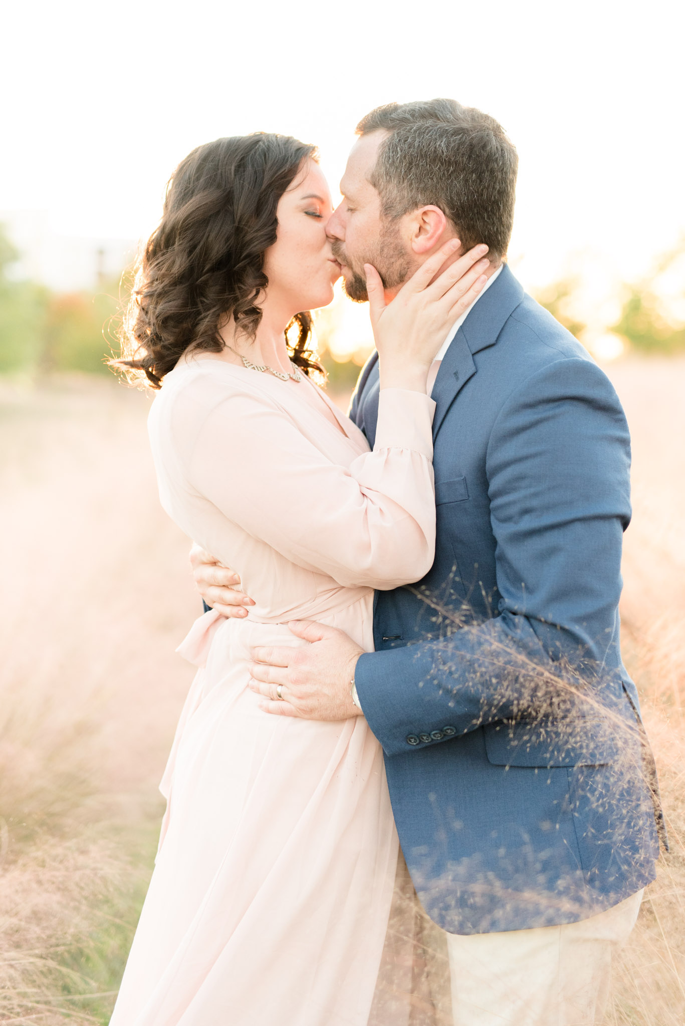 Married couple kiss in field.