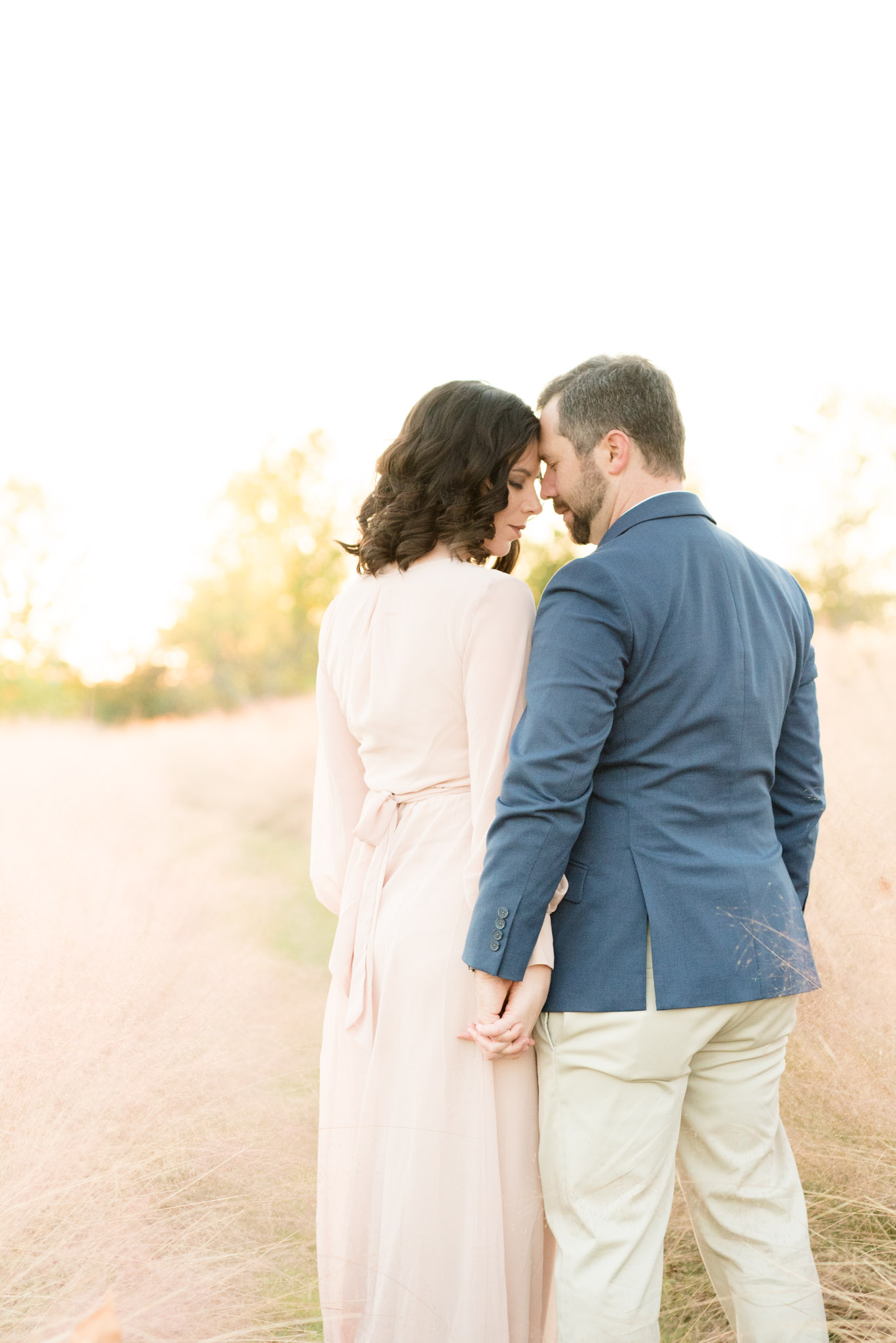 Married couple snuggles in field of tall grass.