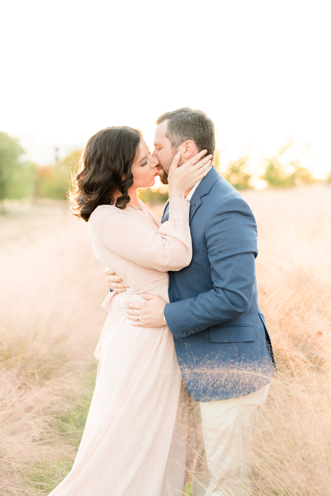 Couple kisses in field of pink grass.