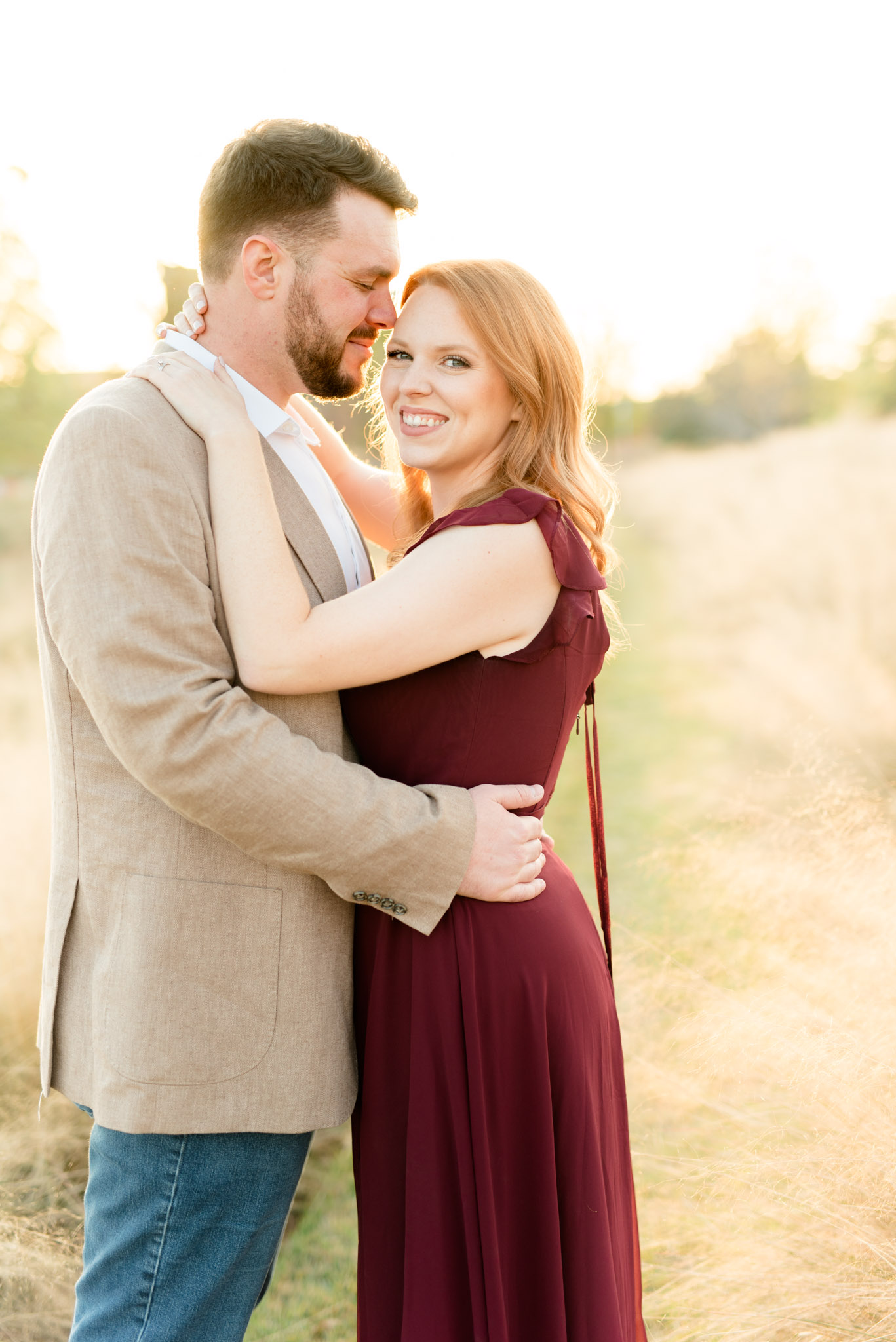 Married couple snuggles in field at sunset.