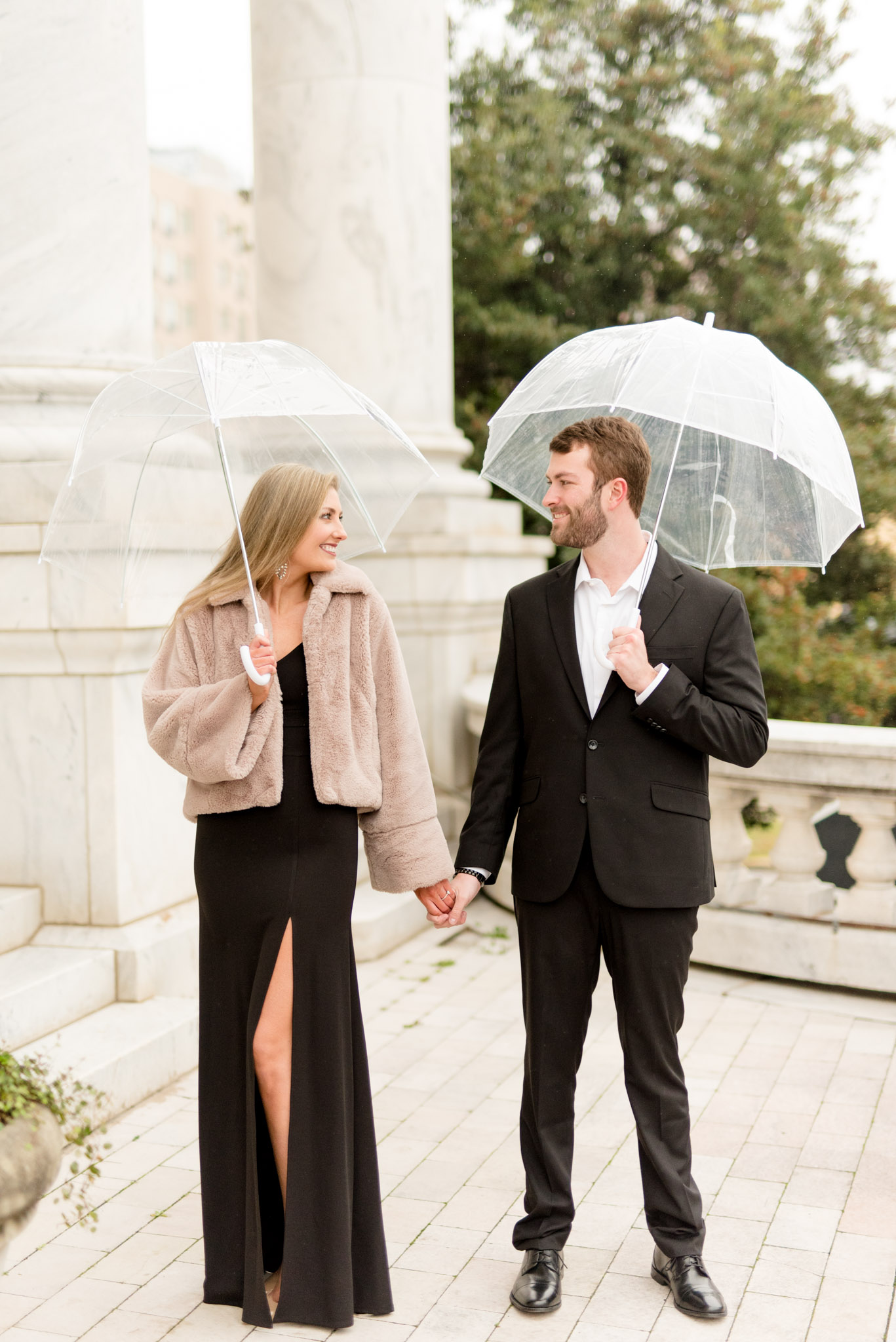 Couple hold hands and umbrellas.