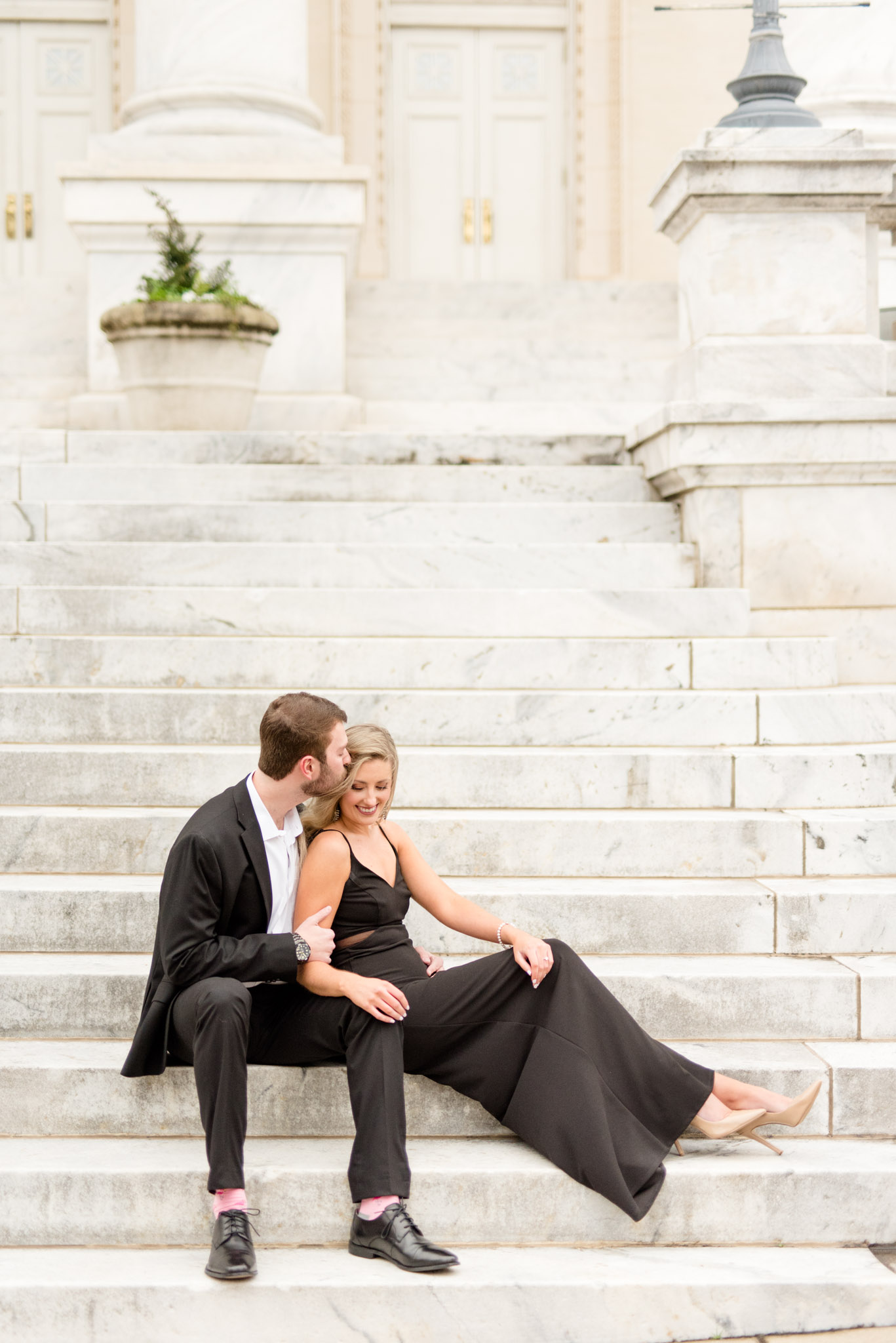 Couple snuggles on marble stairs.