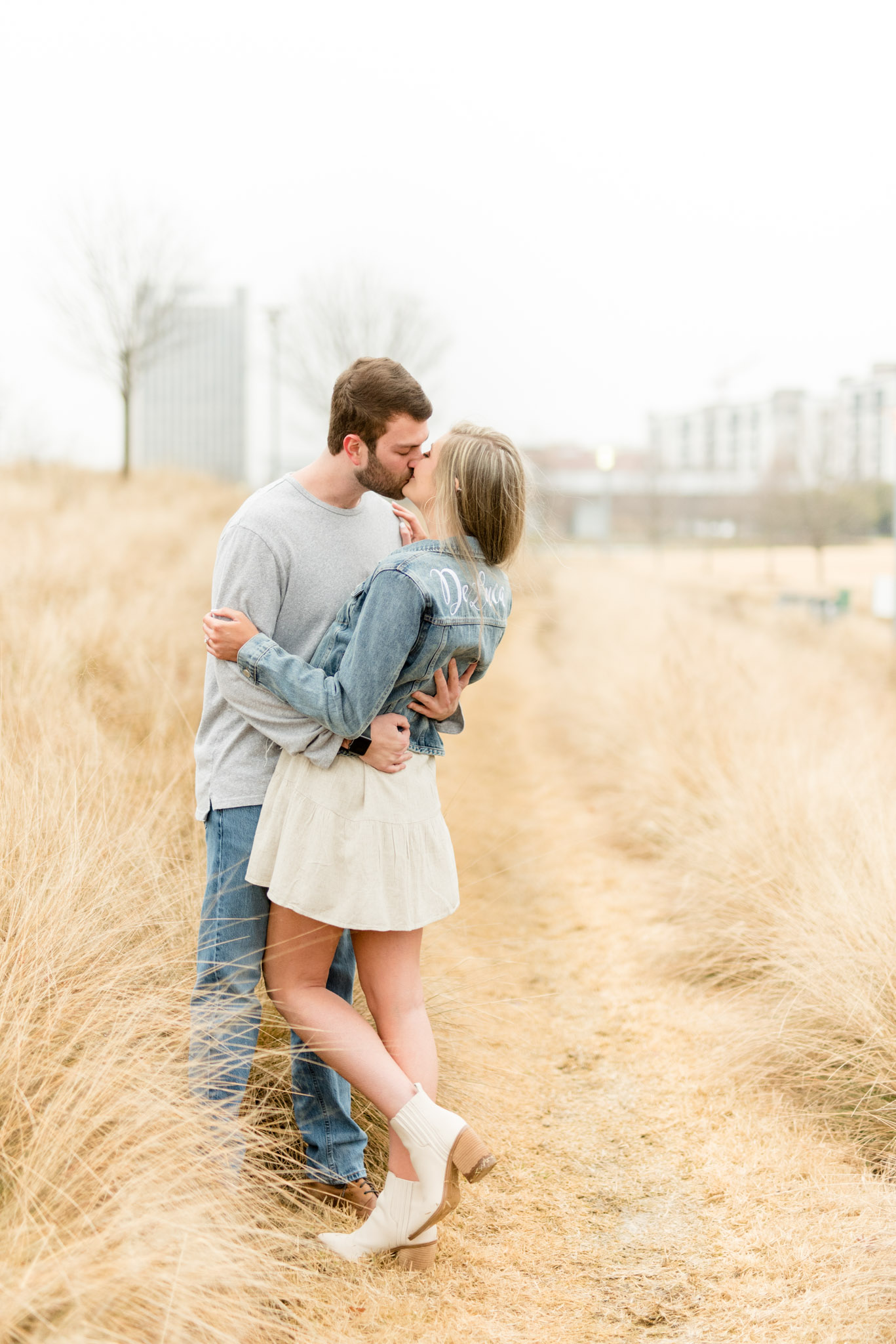 Couple kisses in tall grass field.