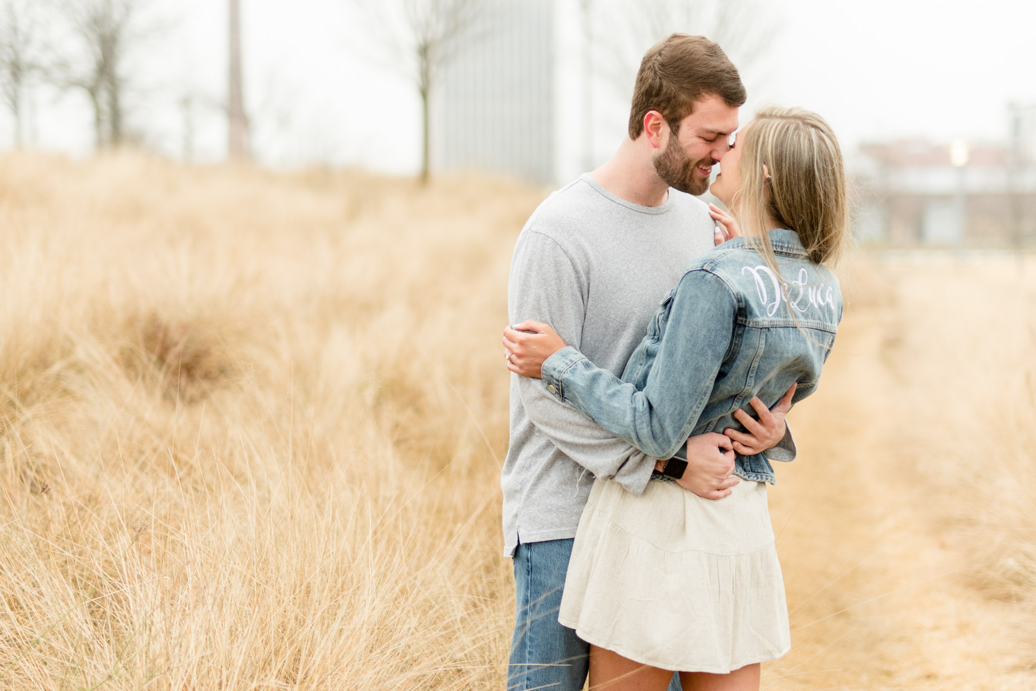Couple leans in for kiss in field.