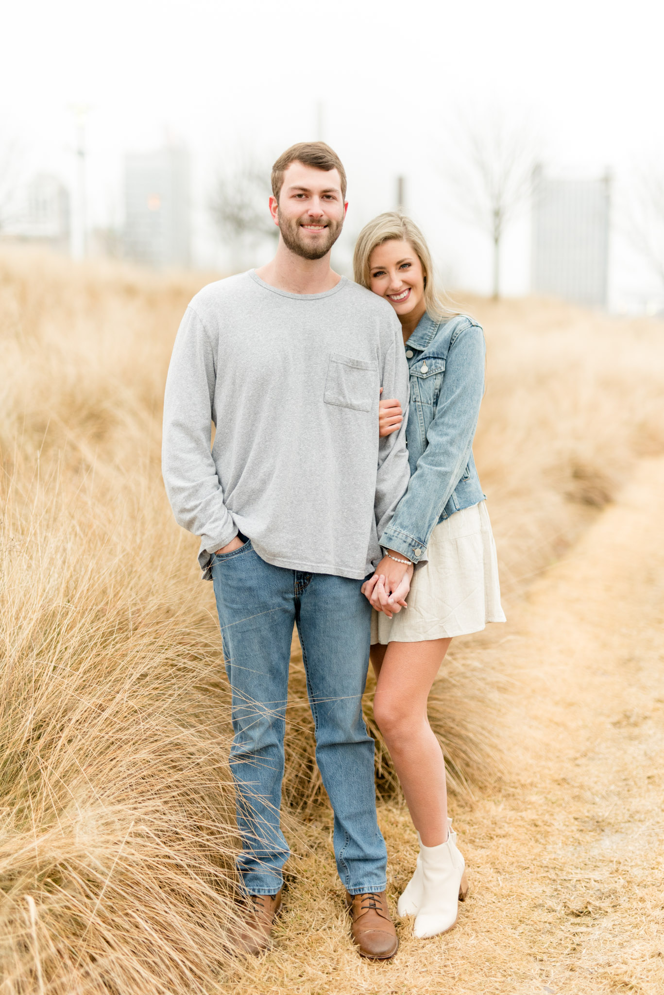 Couple stands in field and smiles at camera.