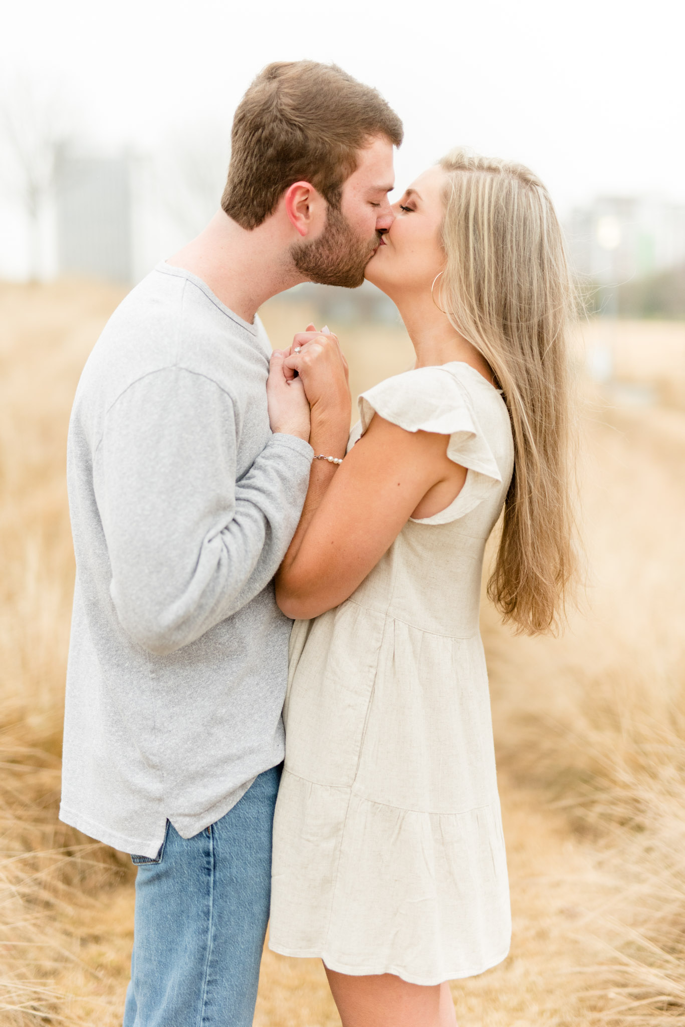 Couple hold hands and kiss in field.