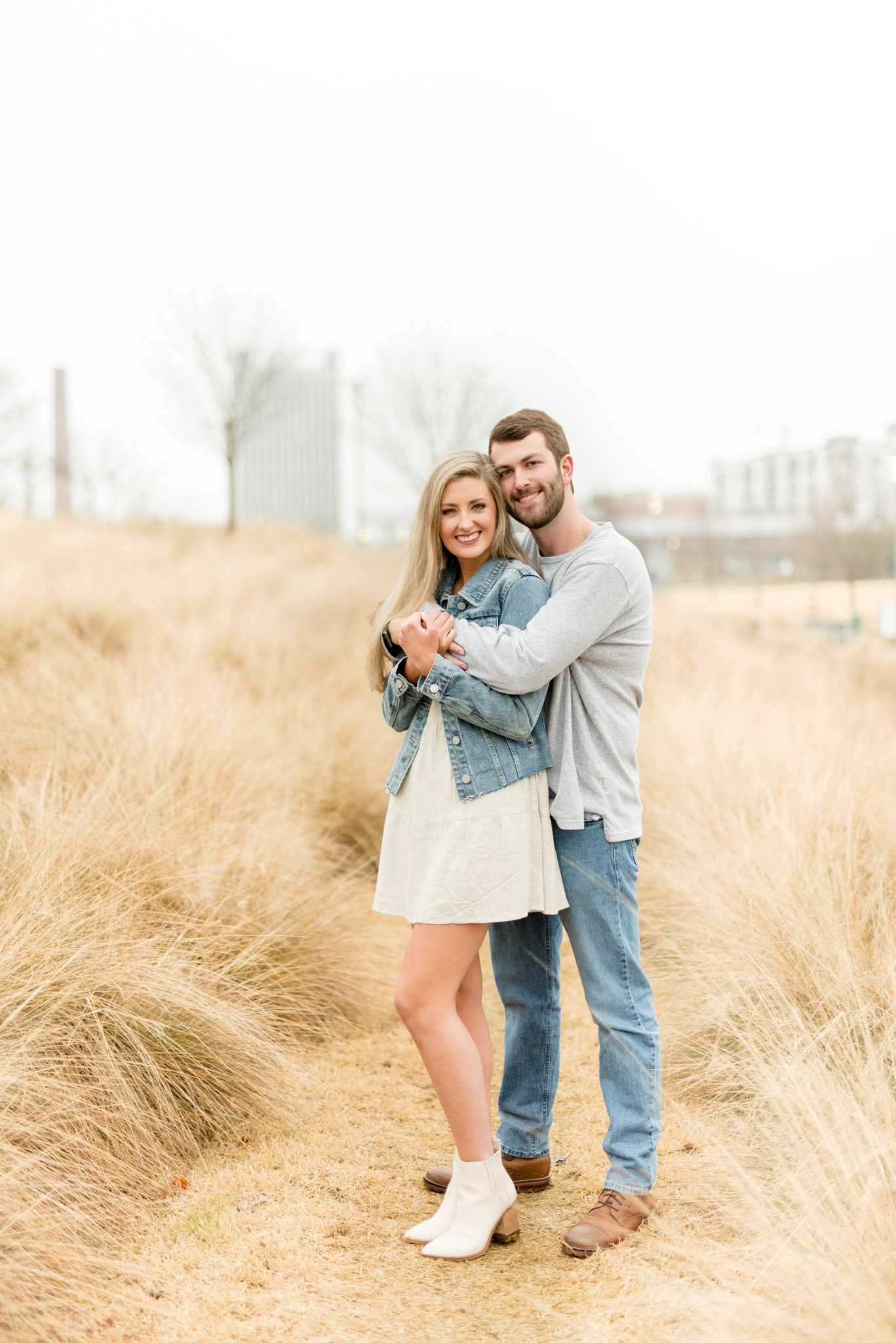 Couple stands in tall grass field and hugs.
