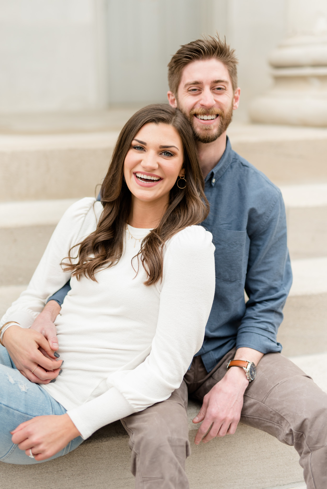 Couple laughs at camera while sitting on stairs.