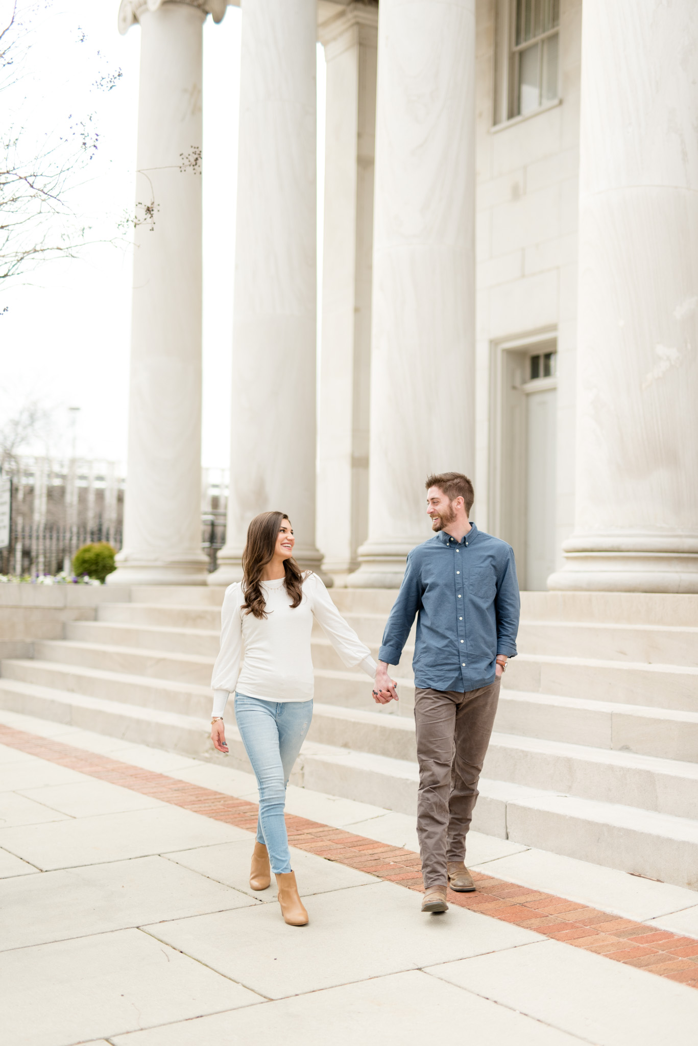 Engaged couple walk in front of columns.