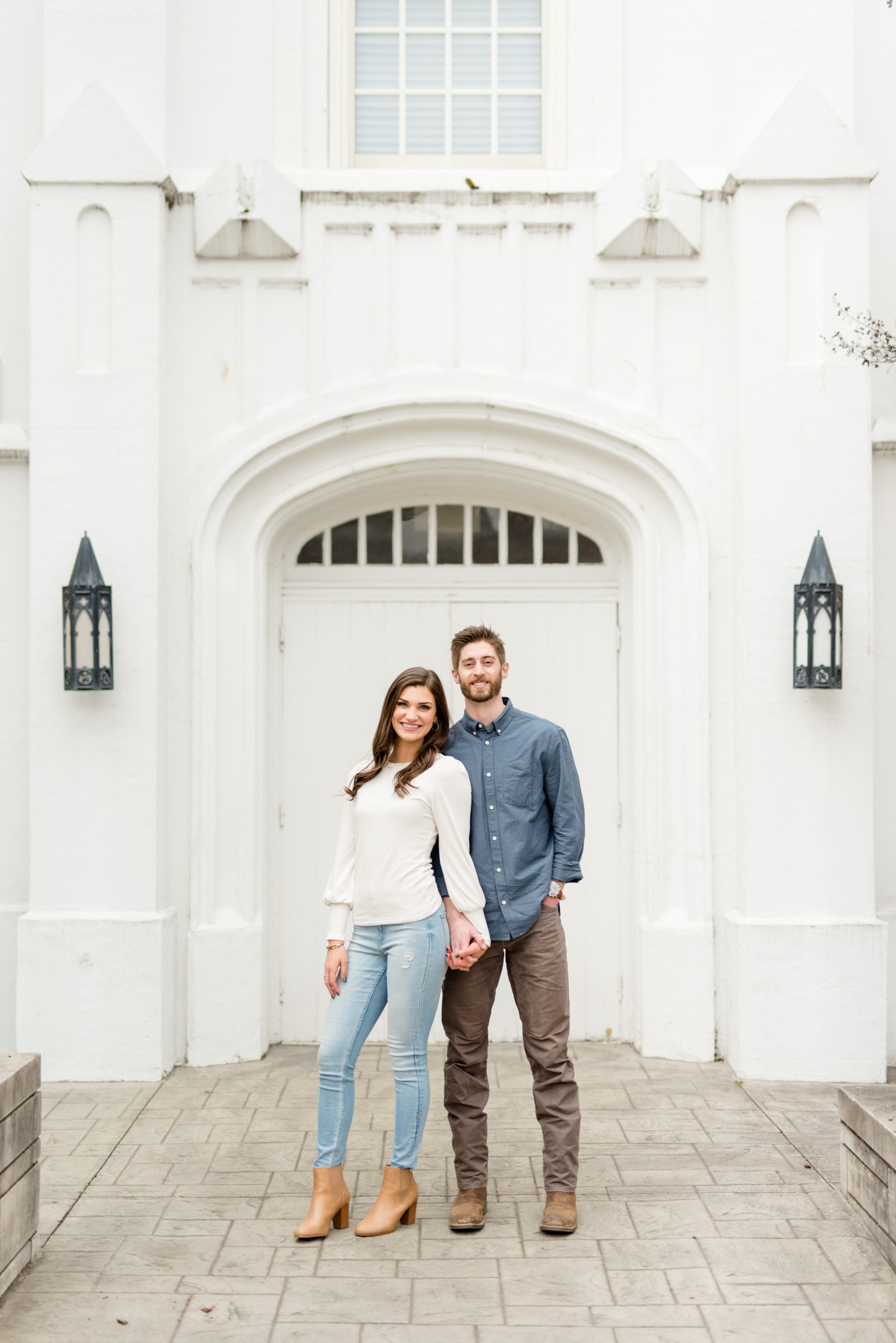 Couple smiles at camera in front of white building.