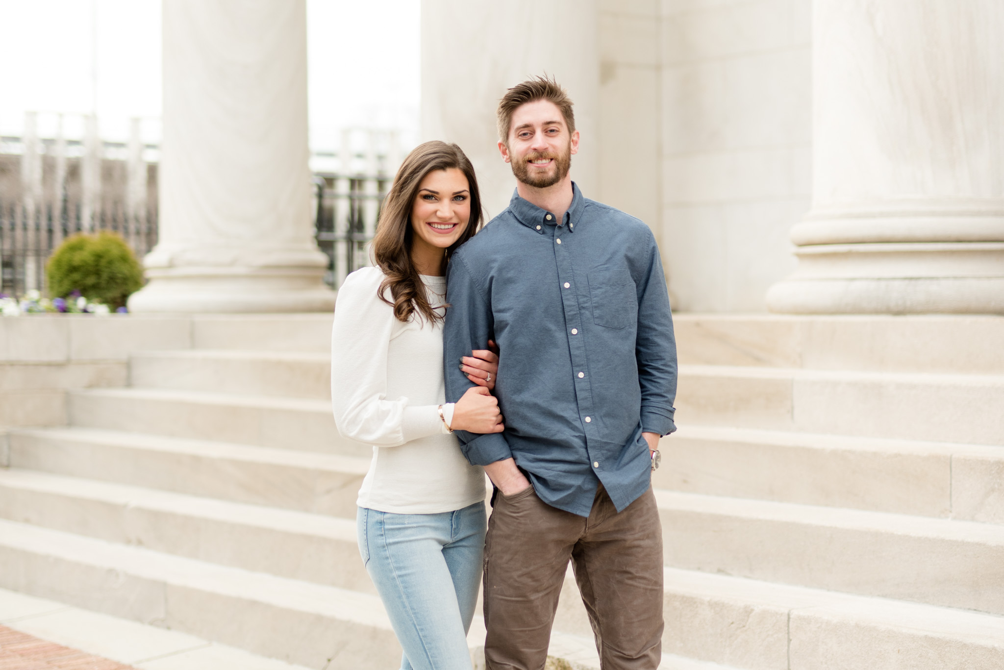 Couple smiles at camera in front of marble staircase.