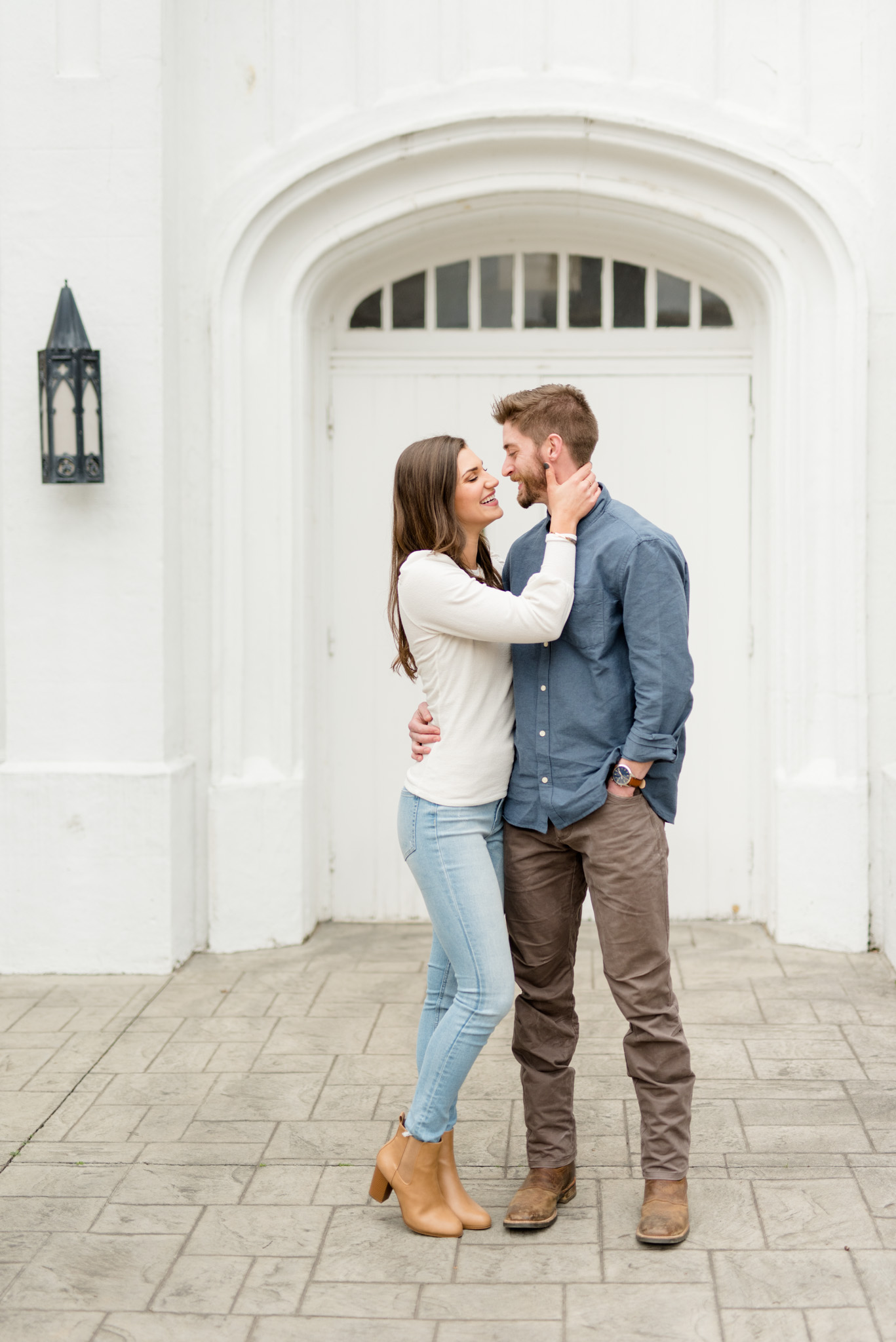 Engaged couple laughs together in front of white door.
