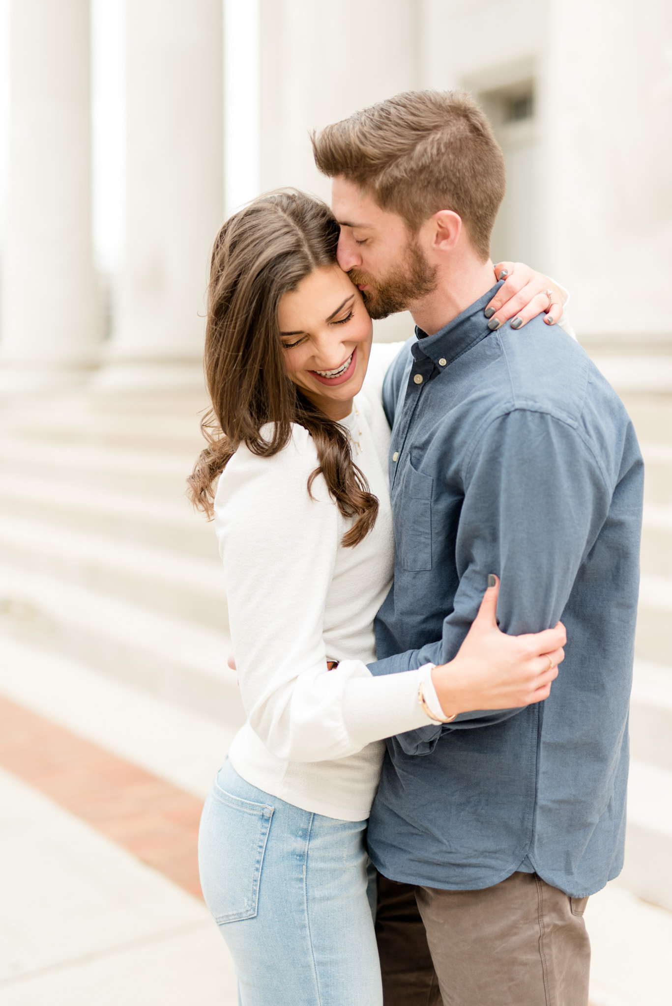Woman laughs as fiancé kisses her temple.