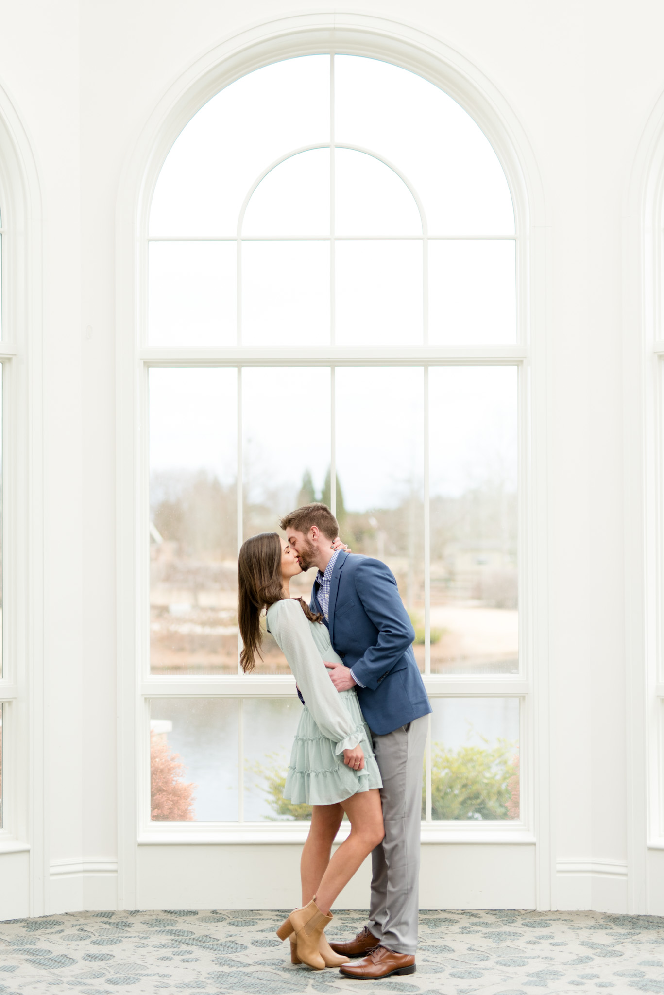 Couple kisses in front of grand window.
